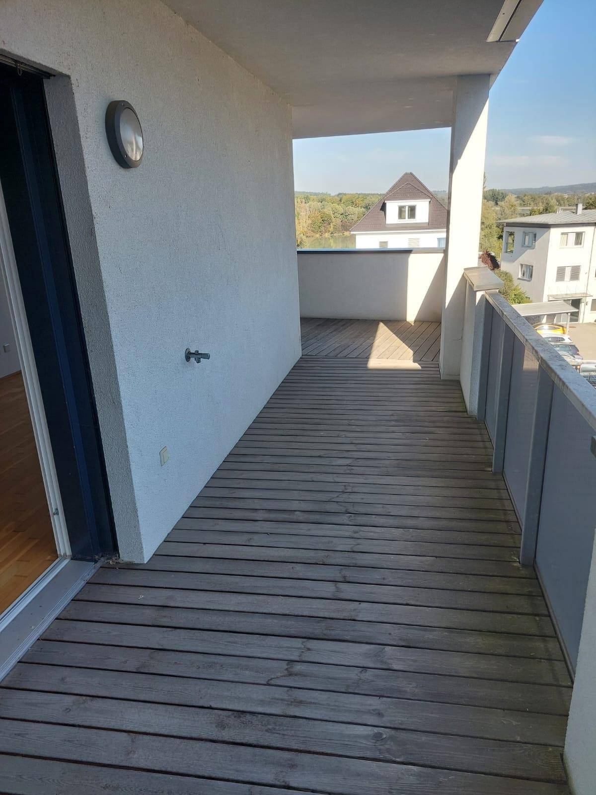 Geräumiger Balkon mit Holzboden und weitem Blick auf die Umgebung und entfernte Hügel.