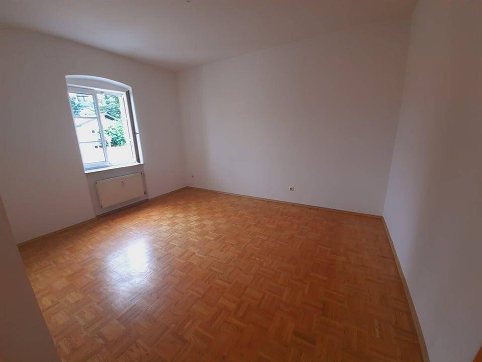 Ruhiges Zimmer mit Parkettboden und einem Fenster, das einen Blick ins Grüne bietet.