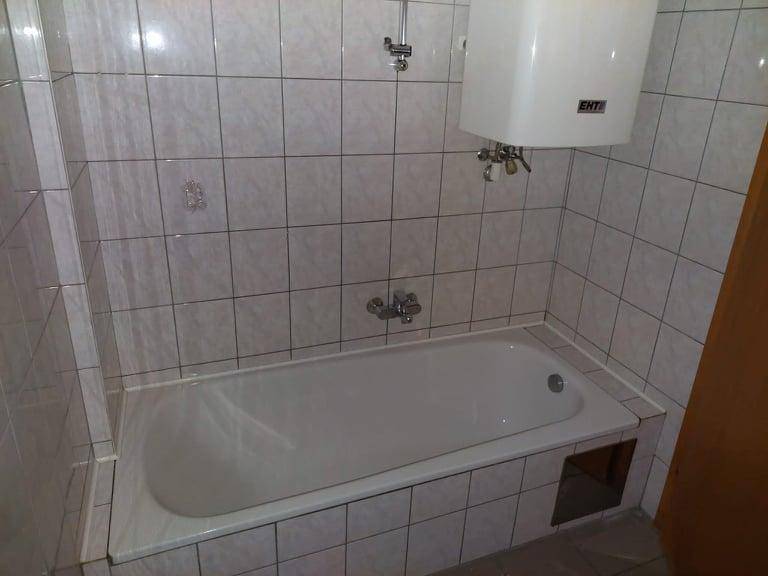 Gefliestes Badezimmer mit Badewanne und Warmwasserboiler an der Wand.