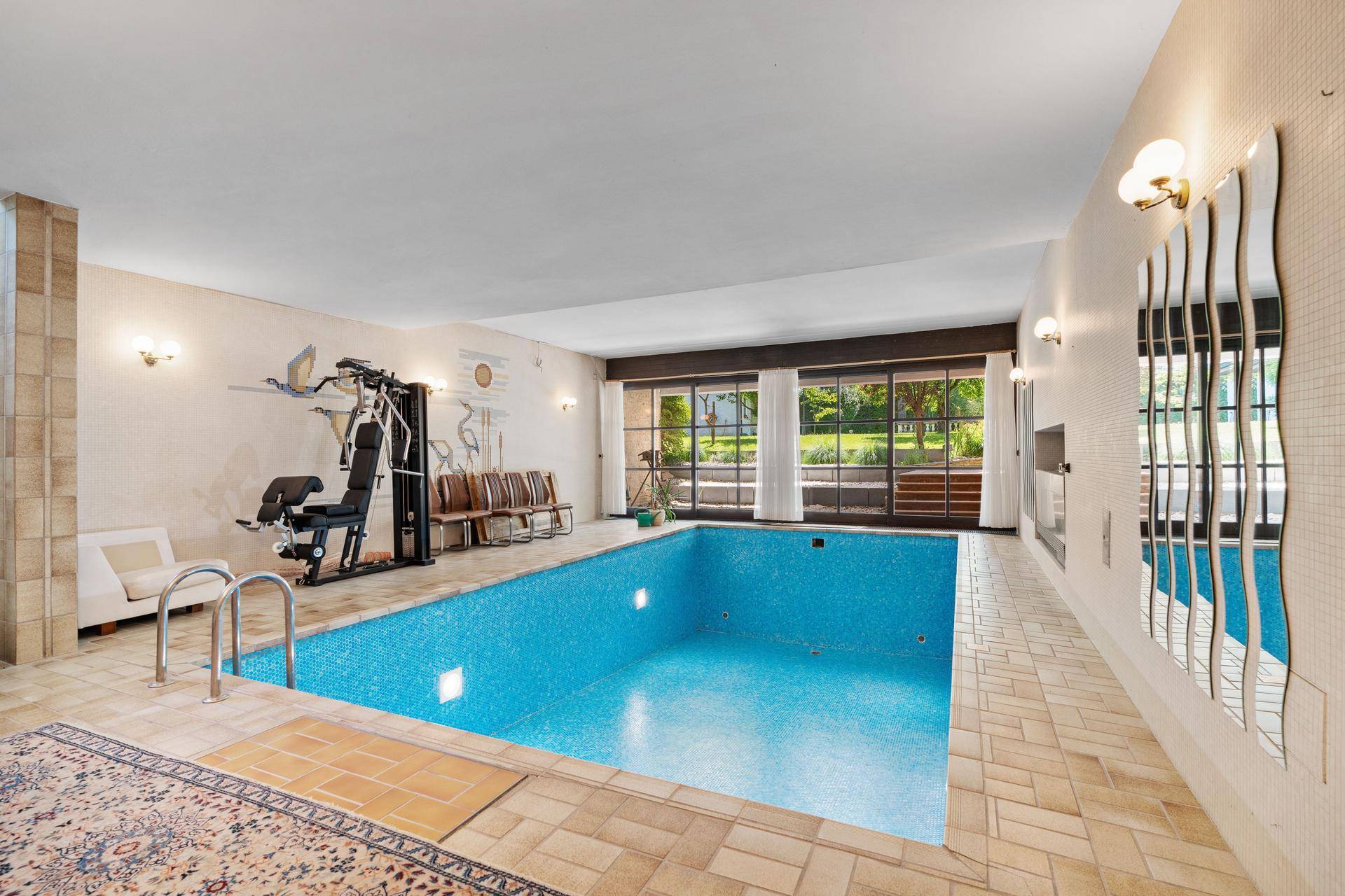 Innenpoolbereich mit Fitnessgeräten, großen Fenstern und direktem Zugang zum Garten.