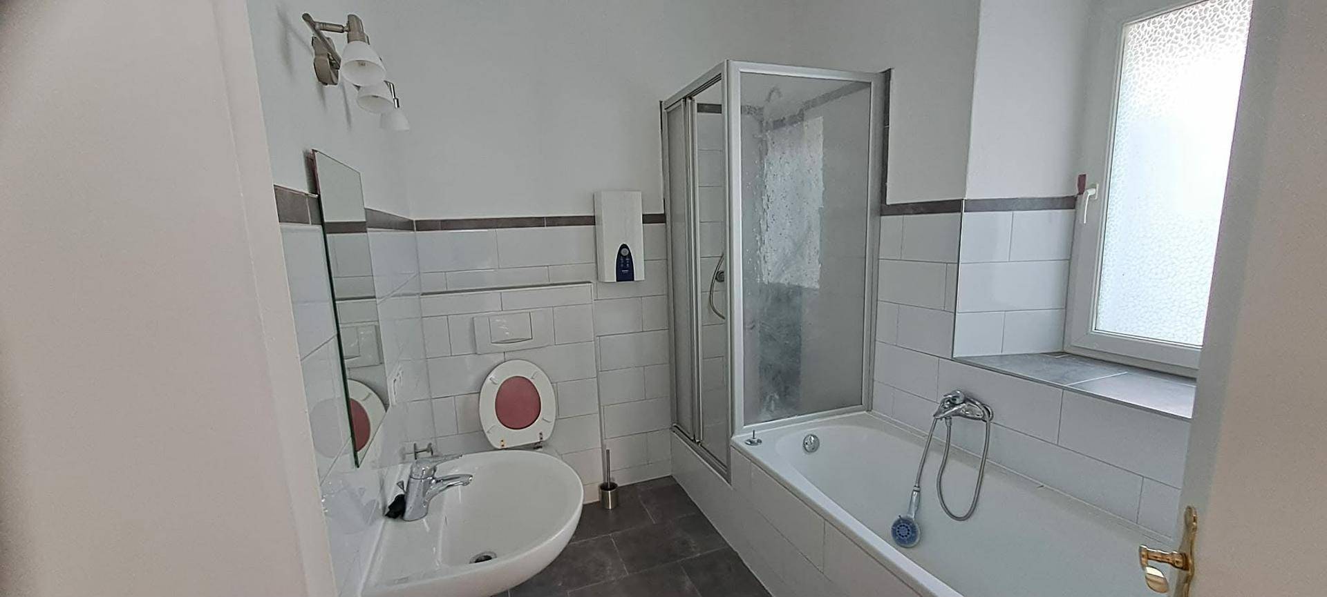Funktionales Badezimmer mit Badewanne, Duschkabine, WC und Fenster für Belüftung.