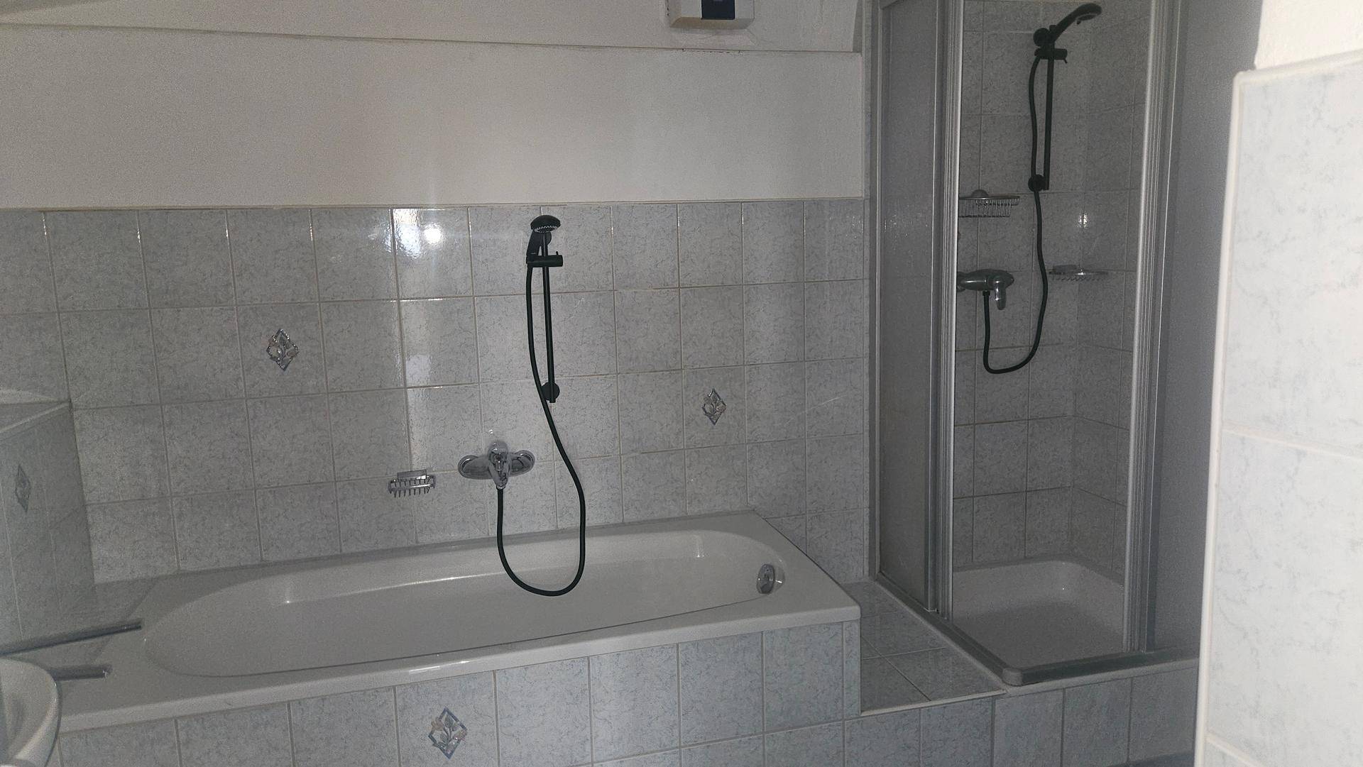 Badezimmer mit Badewanne, separater Duschkabine und hellen Fliesen an Wänden und Boden.