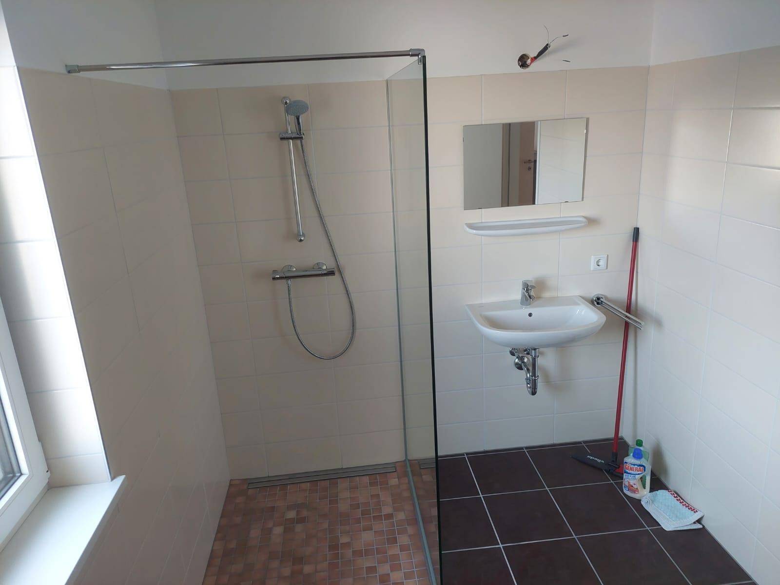 Modernes Badezimmer mit ebenerdiger Dusche, Einzelwaschbecken und hellen Fliesen, ausgestattet mit Haltegriffen.