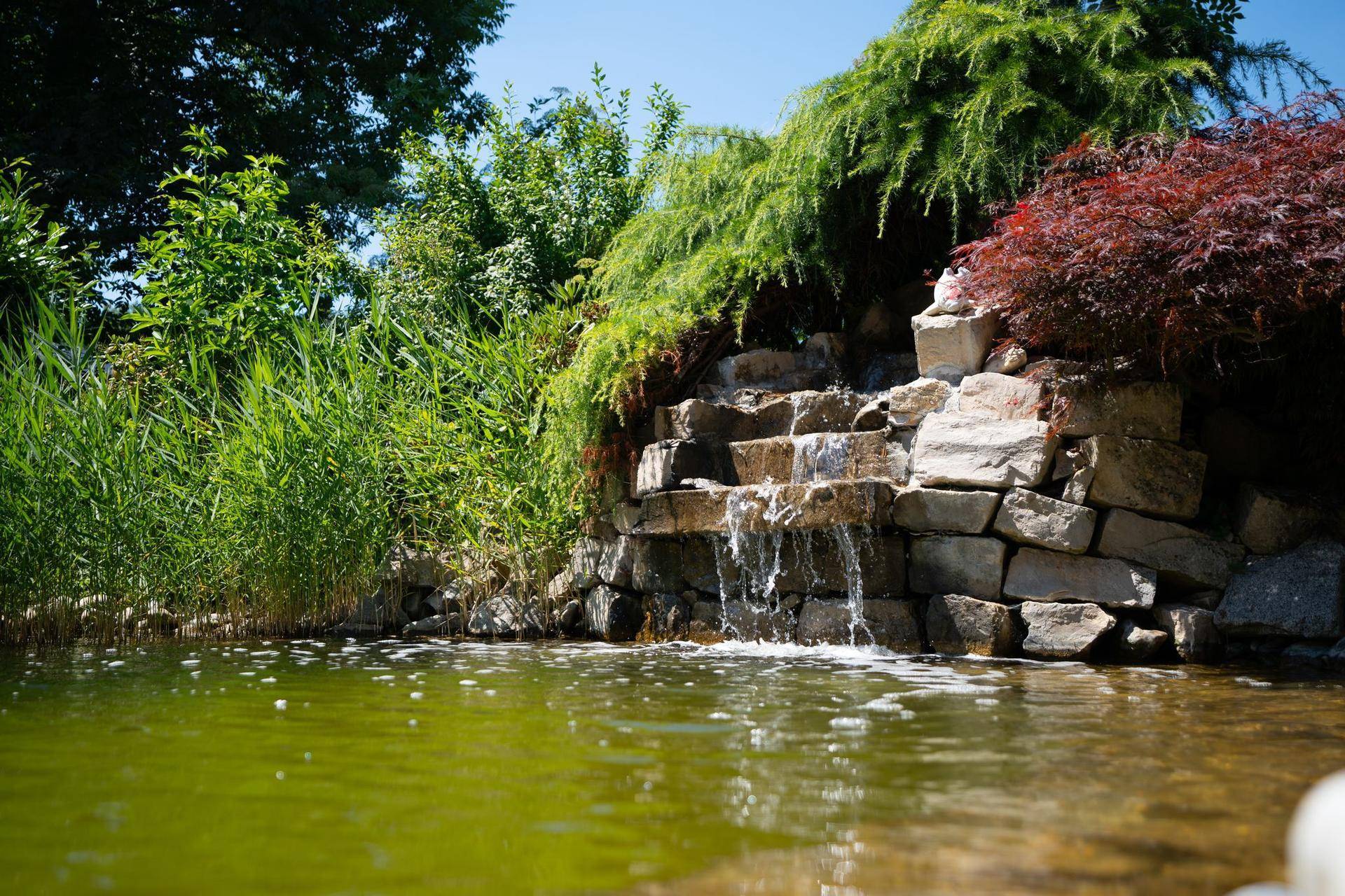 Detailansicht eines künstlichen Wasserfalls aus Steinen, der in einen Teich mündet.
