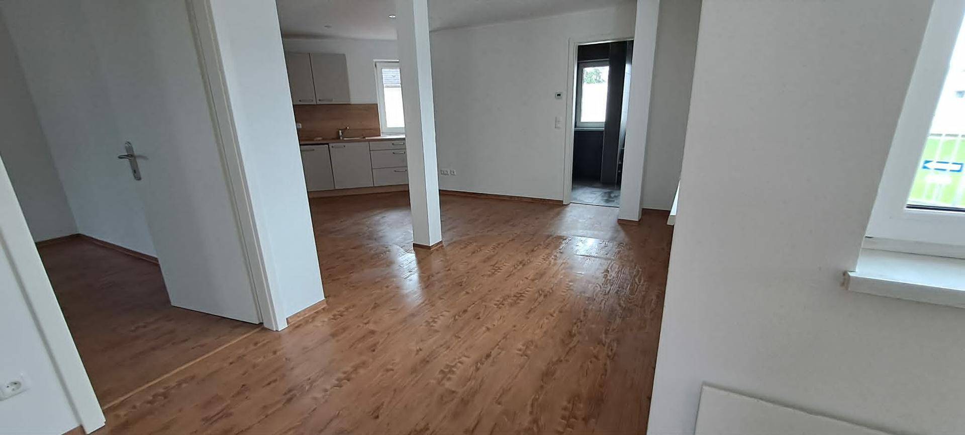 Offener Wohnbereich mit Laminatboden, der in eine moderne Küche übergeht und viel Licht bietet.