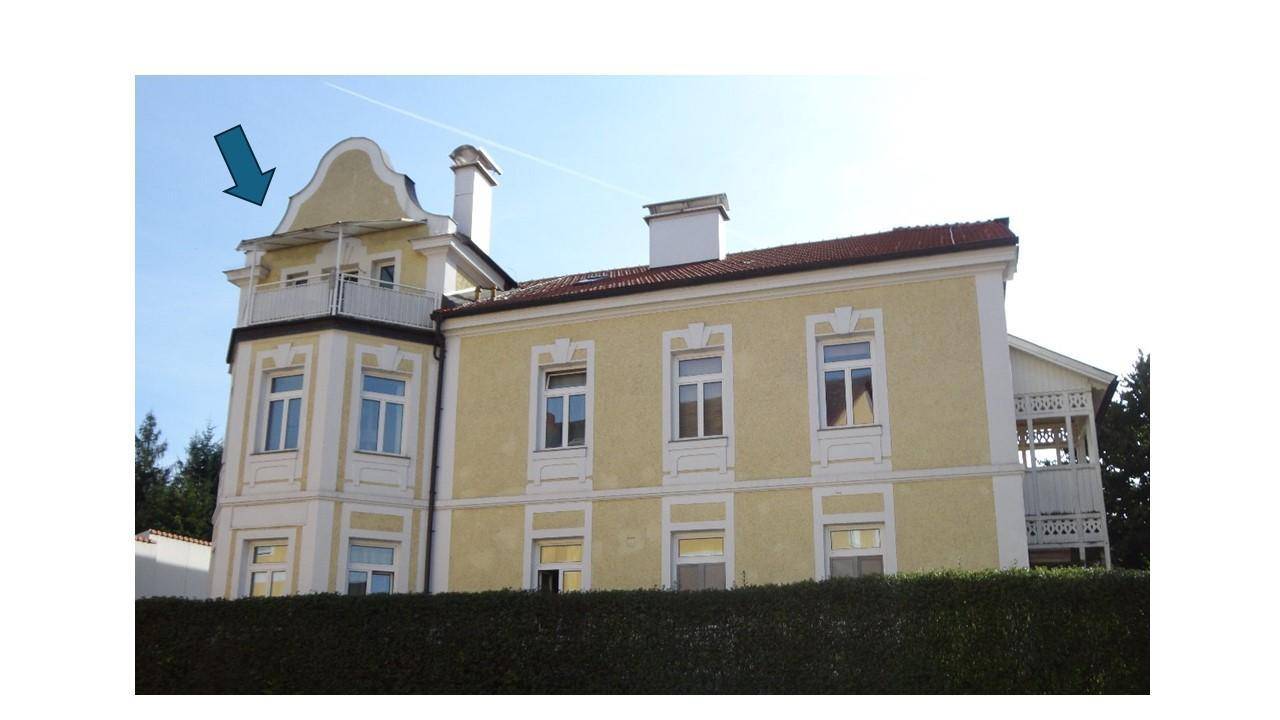 Historisches Gebäude mit gelber Fassade und dekorativen Elementen, umgeben von Grün.