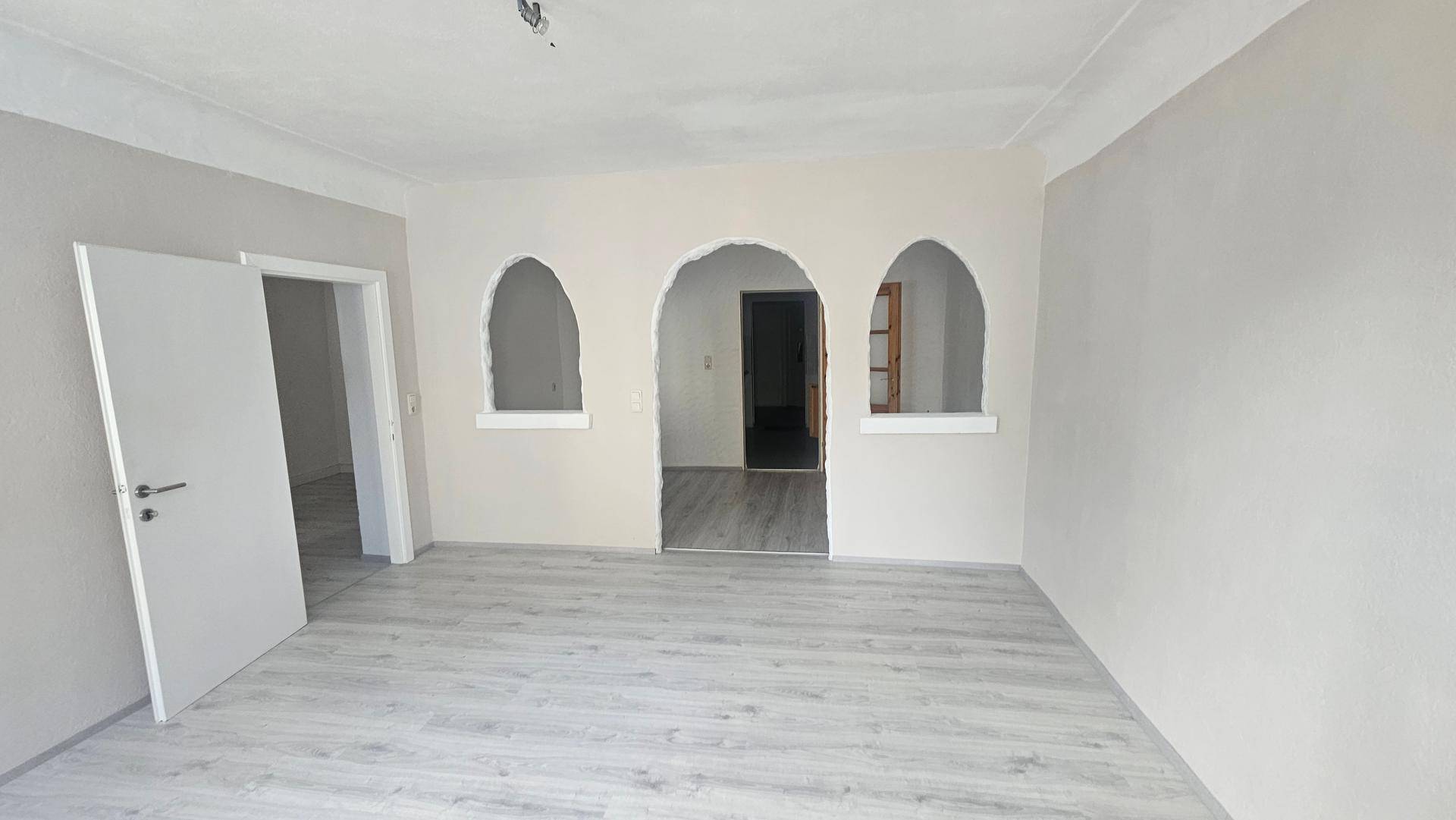 Geräumiges, frisch renoviertes Zimmer mit hellem Laminatboden und charakteristischen Rundbögen.
