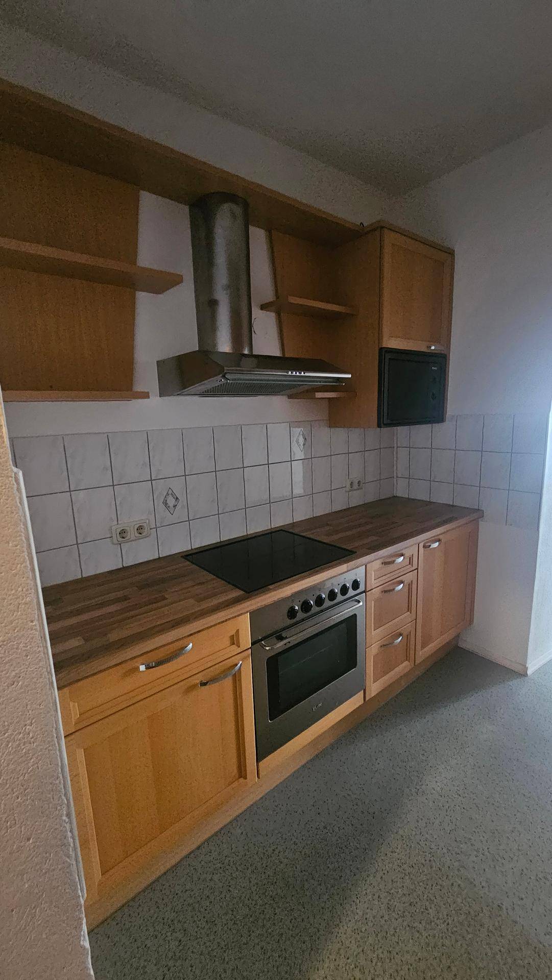 Funktionale Küche mit Holzschränken, integriertem Backofen, Mikrowelle und Dunstabzugshaube.