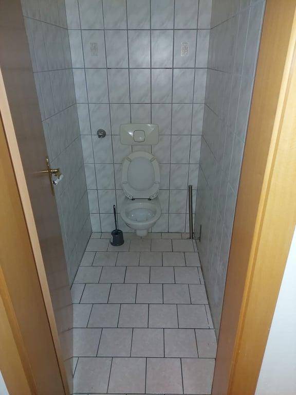 Separates WC mit weißer Fliesenverkleidung und einfacher Toilette.