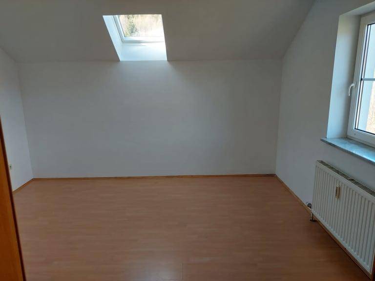 Heller Raum im Dachgeschoss mit Laminatboden, Dachfenster und Heizkörper.