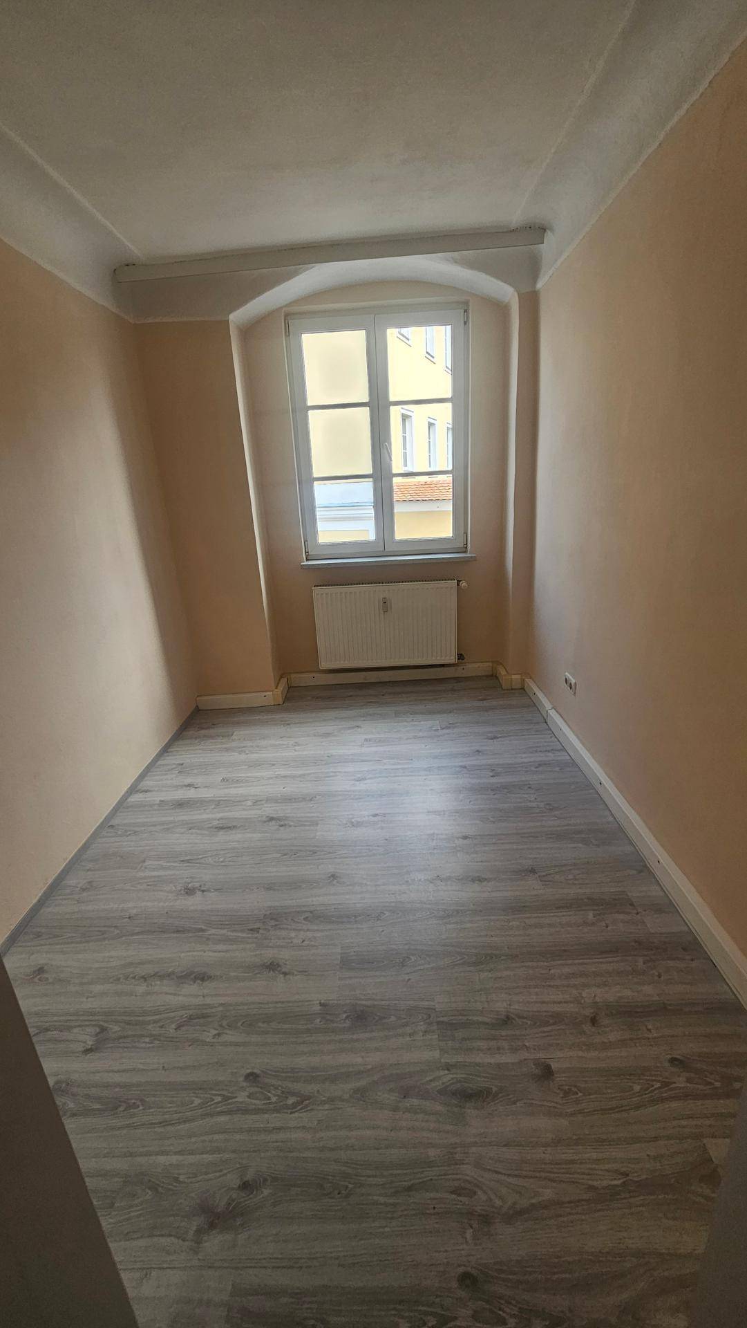 Kleines, helles Zimmer mit einem Fenster, Heizkörper und neu verlegtem Laminatboden.