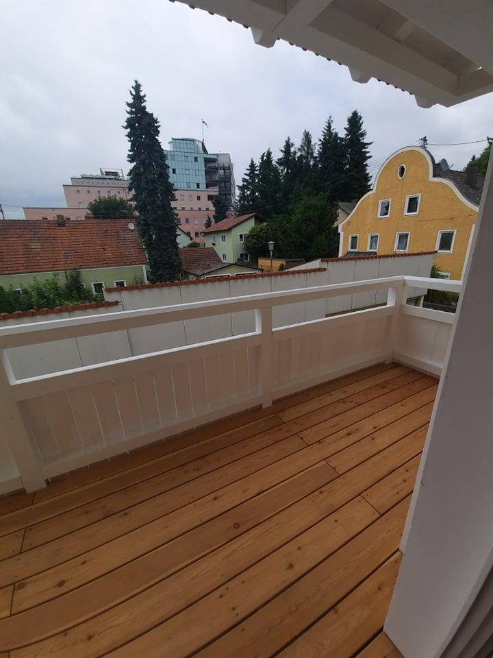 Geräumiger Balkon mit Holzboden und weitem Blick über die Dächer der Stadt.