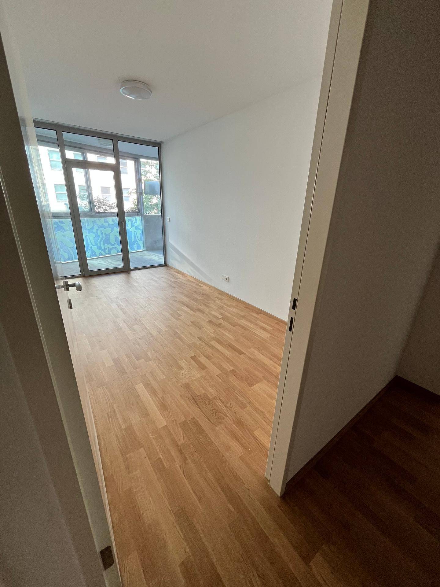 Helles Schlafzimmer mit Parkettboden und Zugang zu einem Balkon oder einer Loggia.
