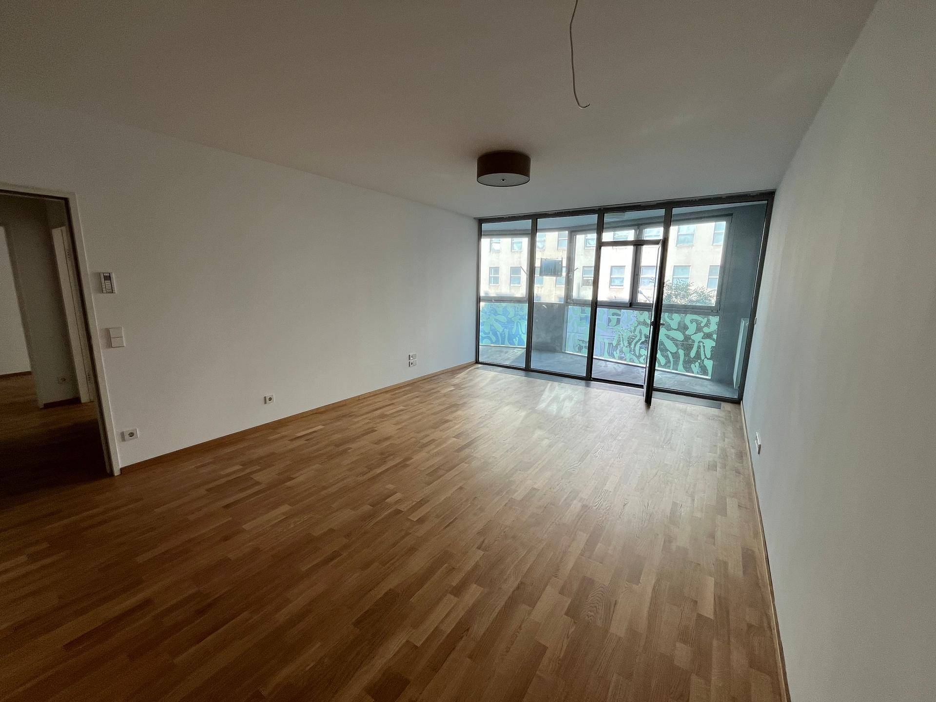 Geräumiger Wohnbereich mit Parkettboden und großen Fenstern, die den Raum mit Tageslicht füllen.