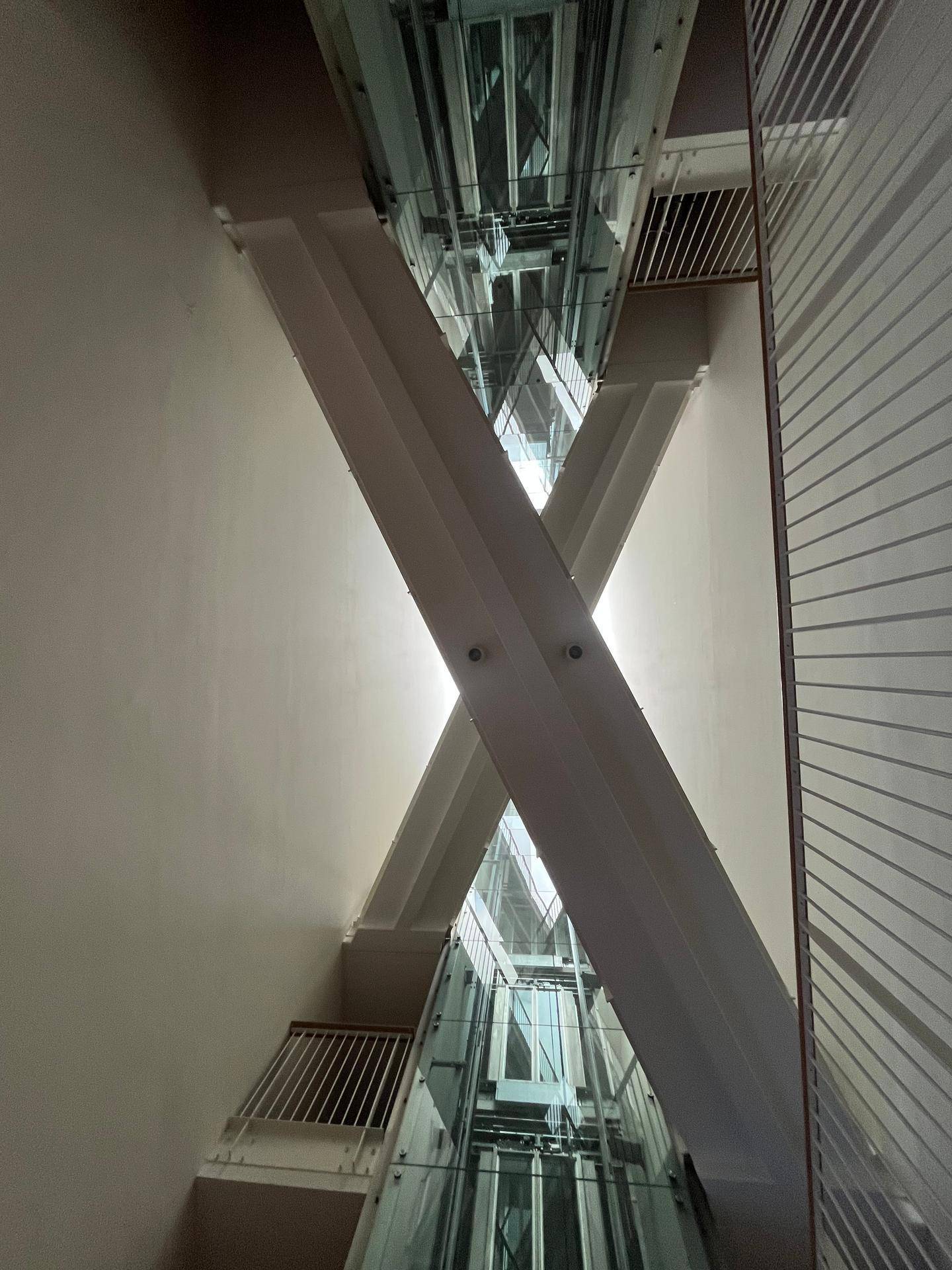 Moderner Glasaufzug in einem hohen Atrium, der die verschiedenen Etagen des Gebäudes verbindet.