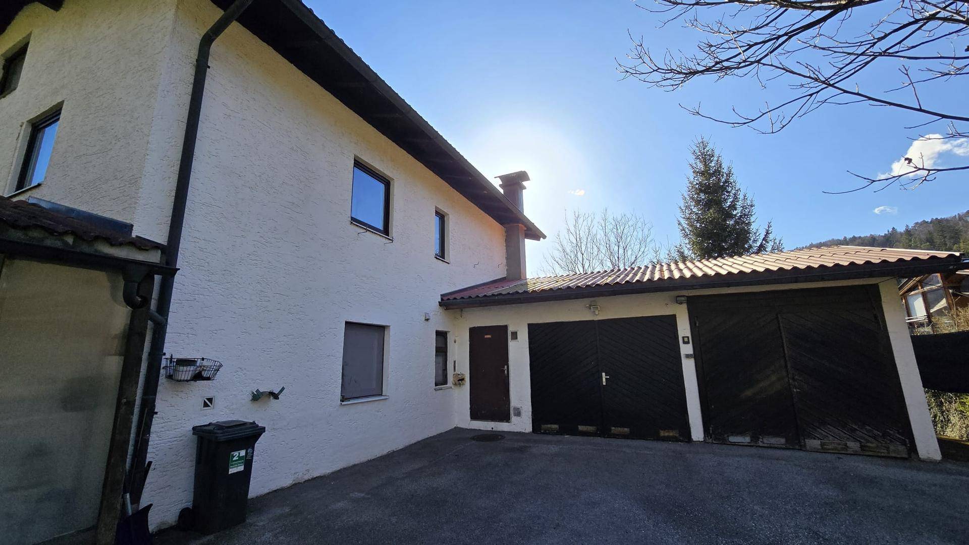 Seitenansicht des Hauses mit zwei Garagen und einem gepflasterten Bereich unter blauem Himmel.