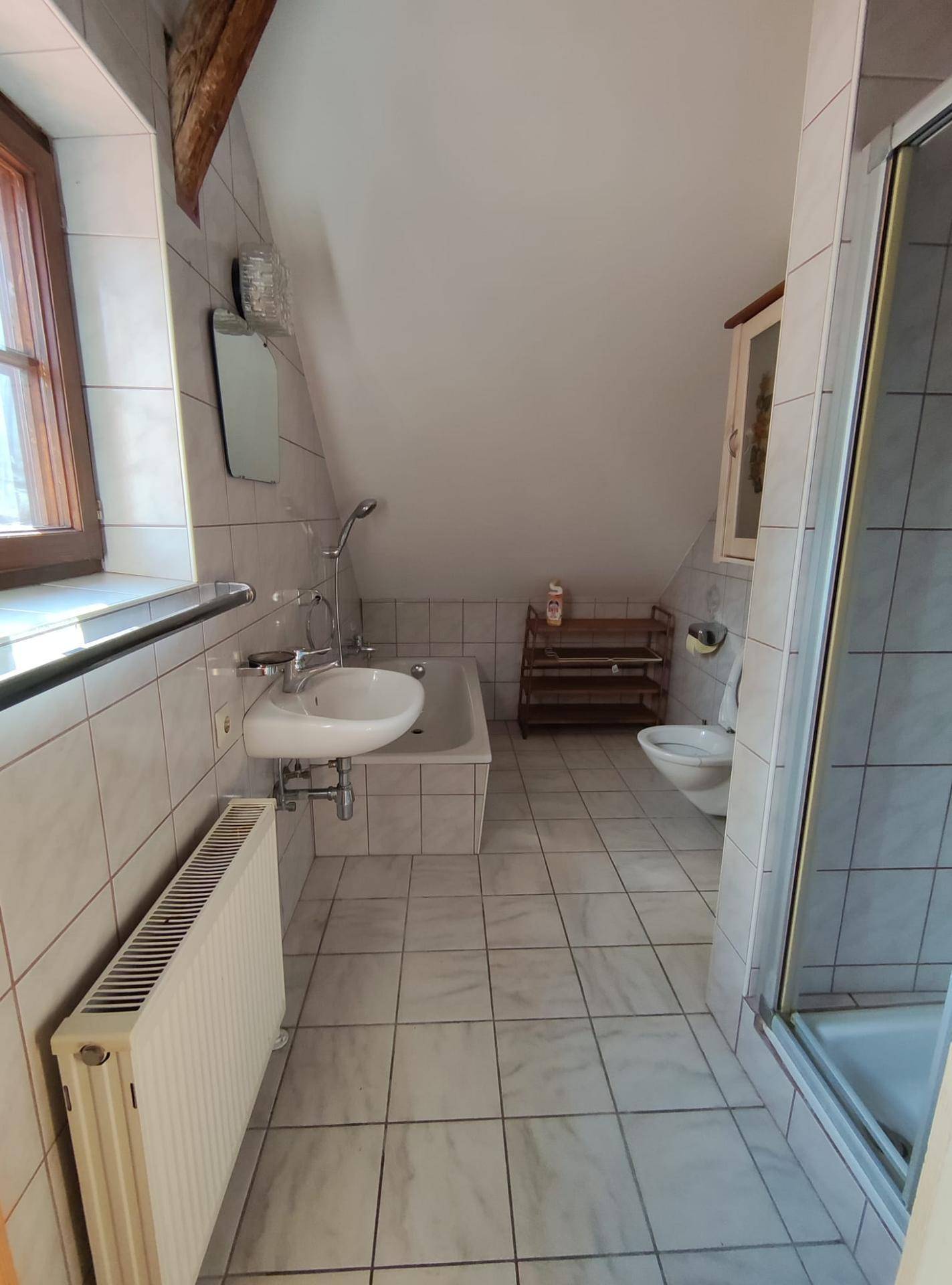 Gefliestes Badezimmer mit Badewanne, Dusche, WC und Fenster unter der Dachschräge.