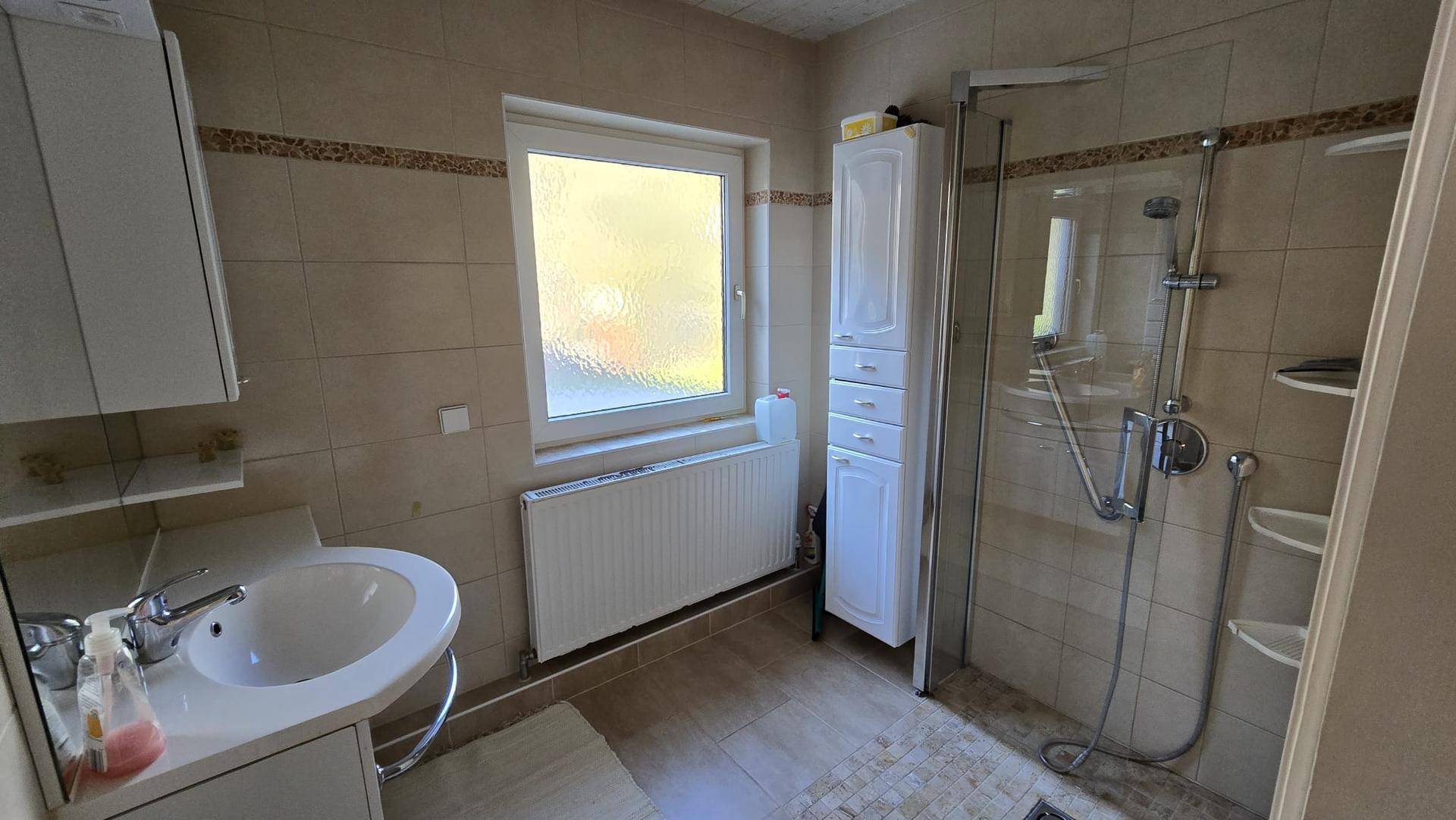 Badezimmer mit beigen Fliesen, Waschbecken, Duschkabine und einem Spiegelschrank.