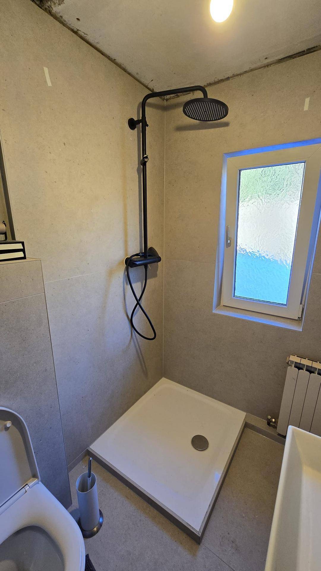 Badezimmer im Rohbau mit Duschbereich, Wand-WC und einer modernen schwarzen Regendusche.