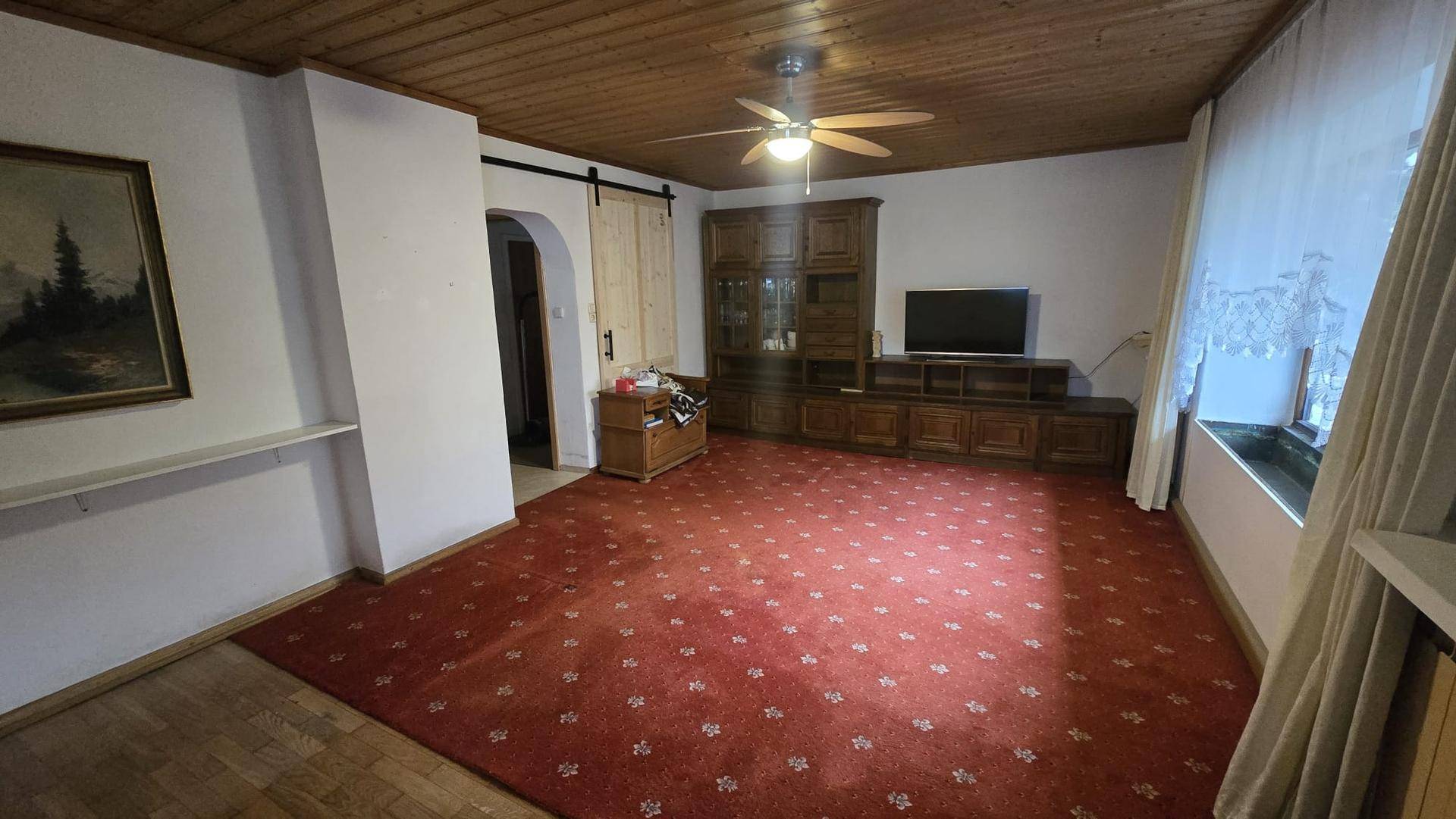 Geräumiges Wohnzimmer mit Holzdecke, rotem Teppich und traditionellen Holzmöbeln.