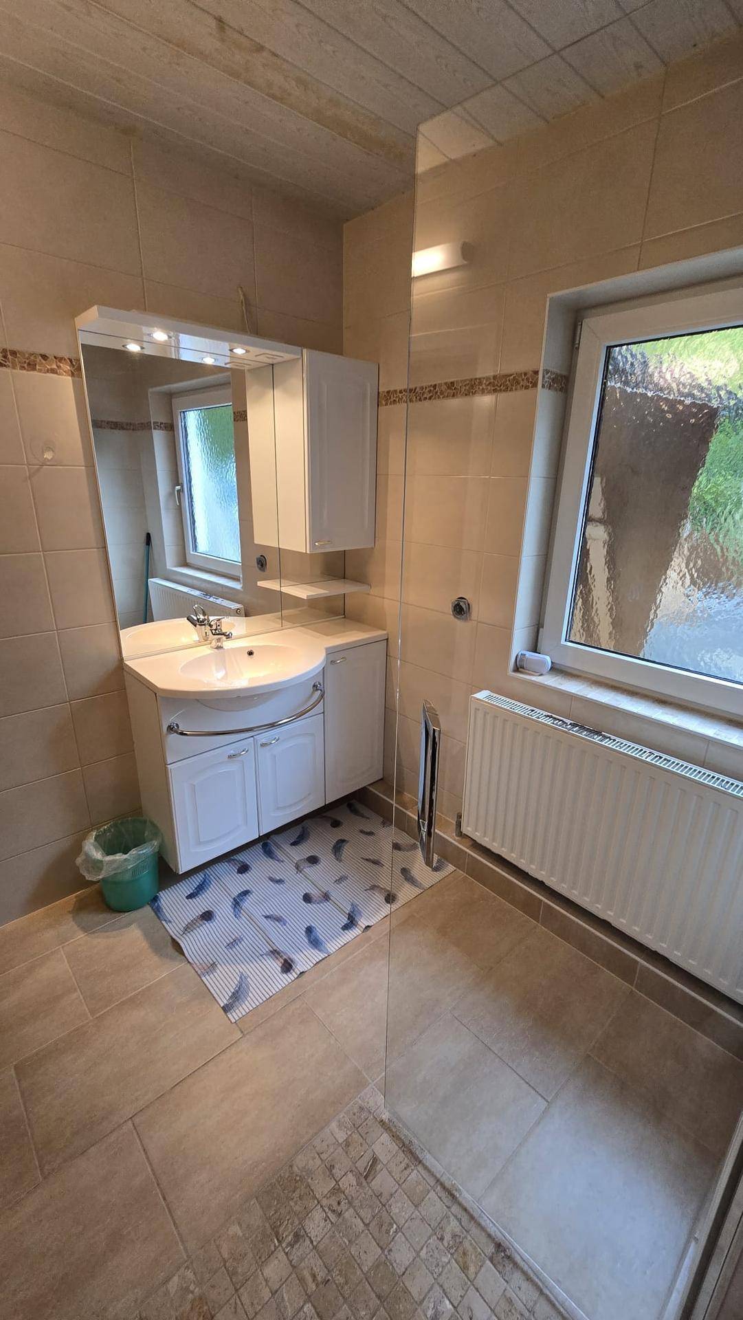 Badezimmer mit beigen Fliesen, Waschbecken, Spiegelschrank und einer Duschkabine.
