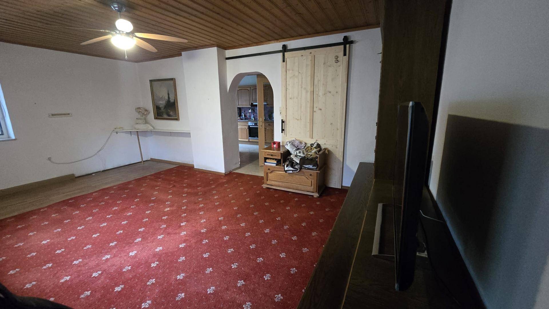 Gemütliches Wohnzimmer mit Holzdecke, rotem Teppich und einem Deckenventilator.