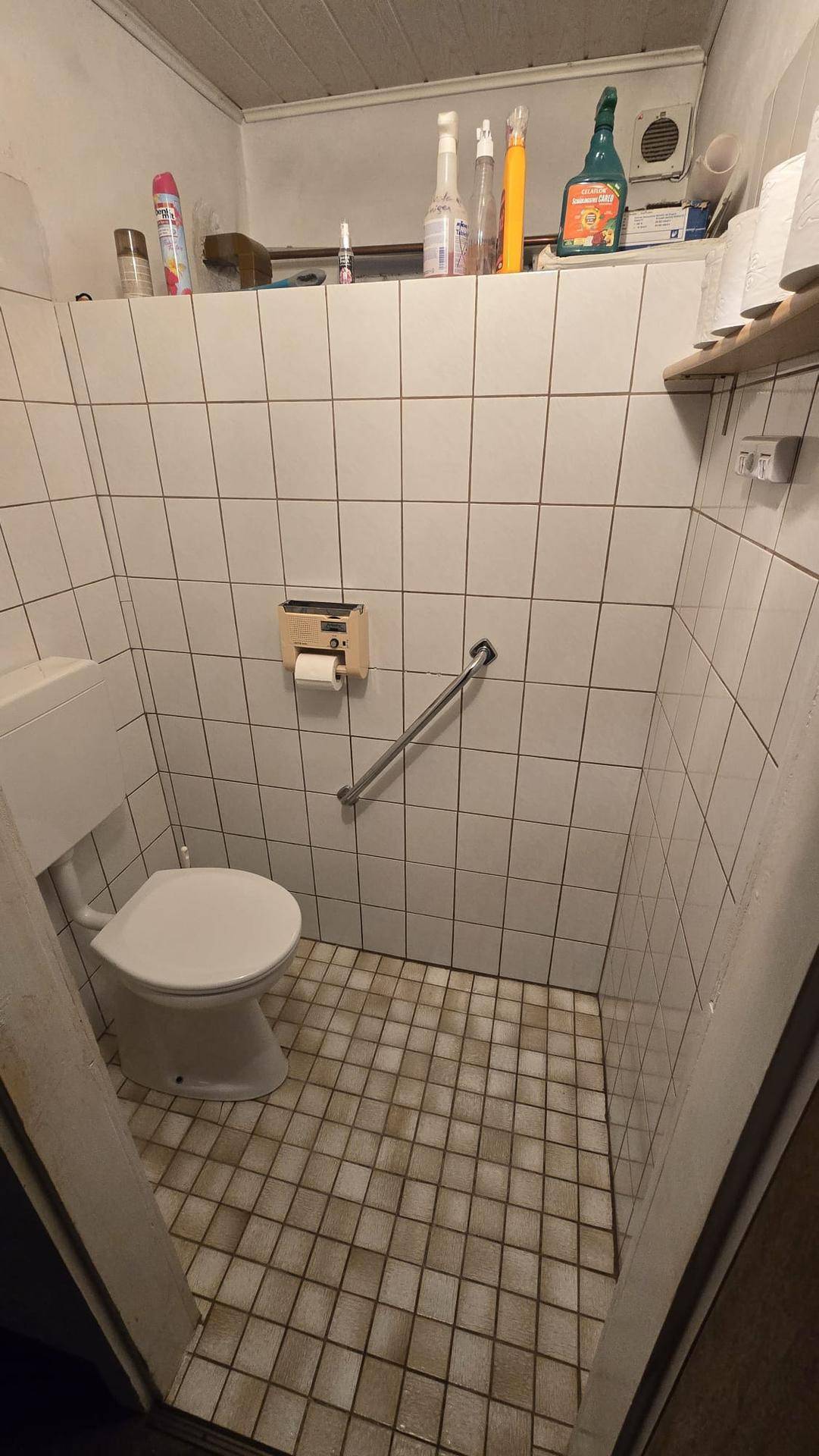 Kleines WC mit weißen Fliesen, Toilette und Haltegriff für zusätzliche Sicherheit.
