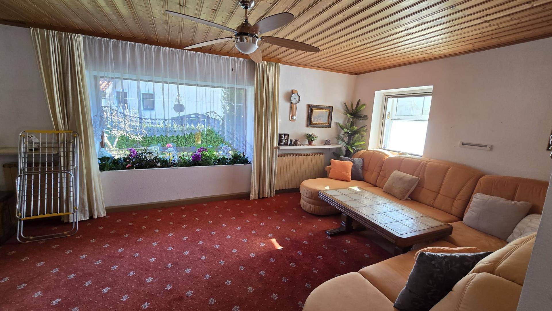 Gemütliches Wohnzimmer mit Holzdecke, rotem Teppich und einer großen Eckcouch.