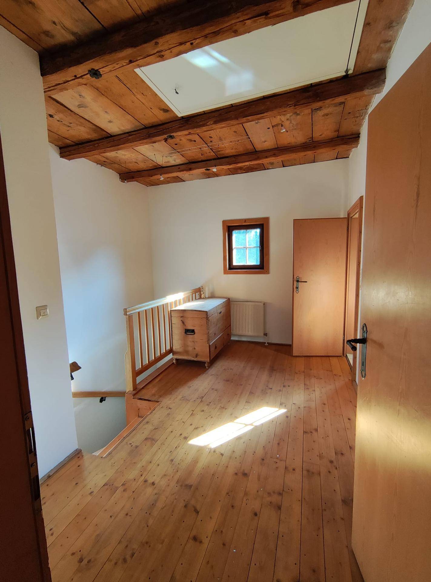 Heller Flurbereich mit Holzboden, sichtbaren Deckenbalken und Zugang zu den unteren Etagen.