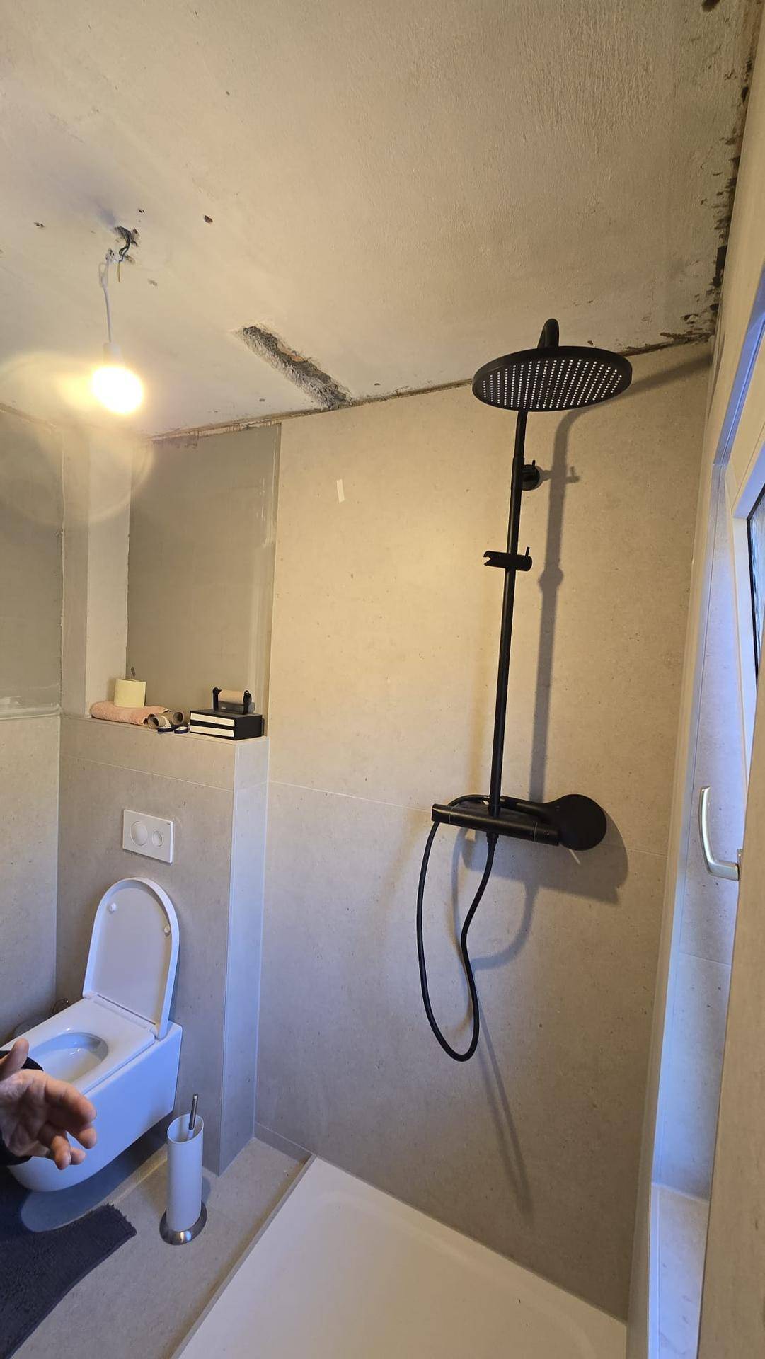 Badezimmer im Rohbau mit Duschbereich, Wand-WC und einer modernen schwarzen Regendusche.
