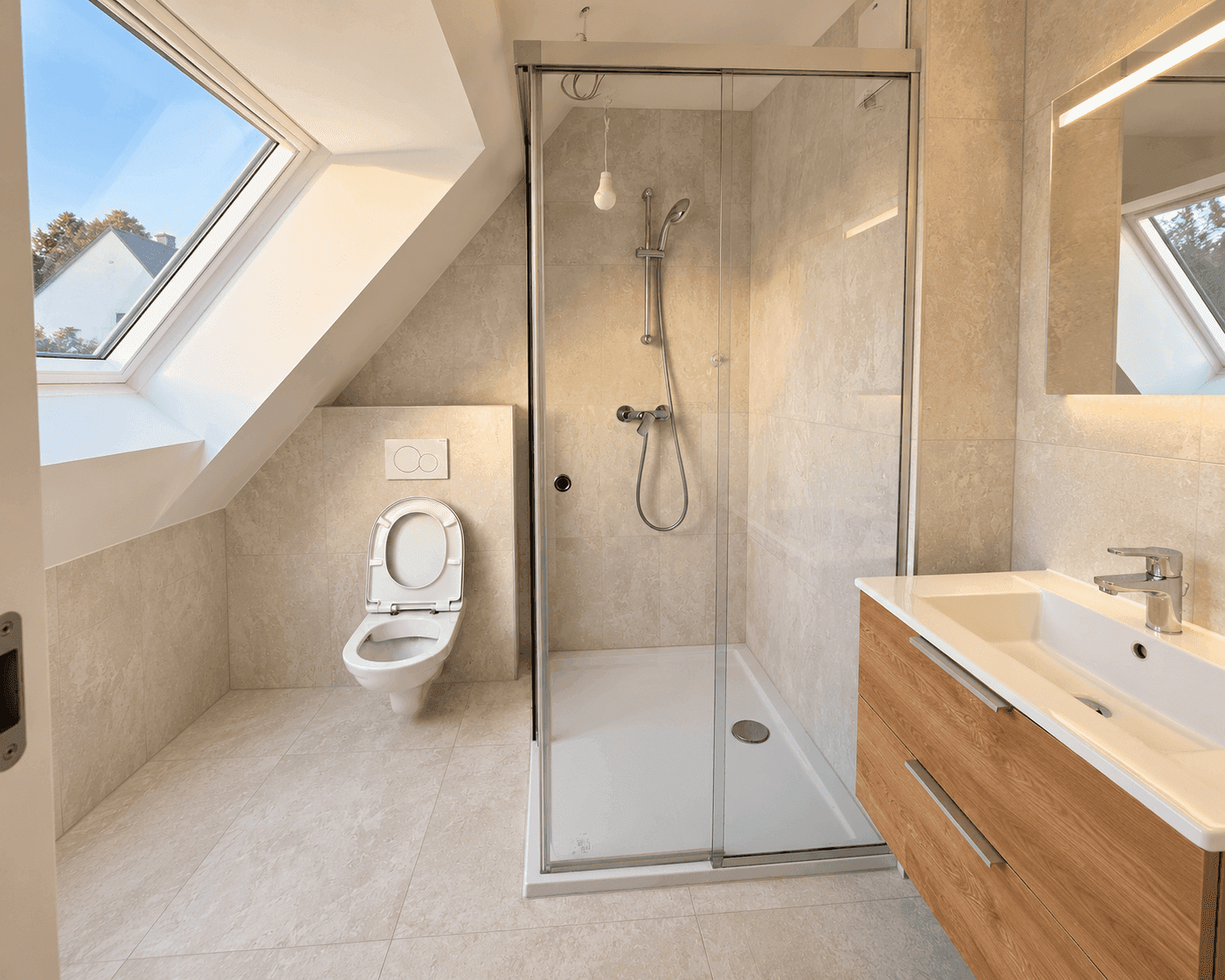 Modernes Badezimmer im Dachgeschoss mit Dusche, WC und großem Dachfenster.
