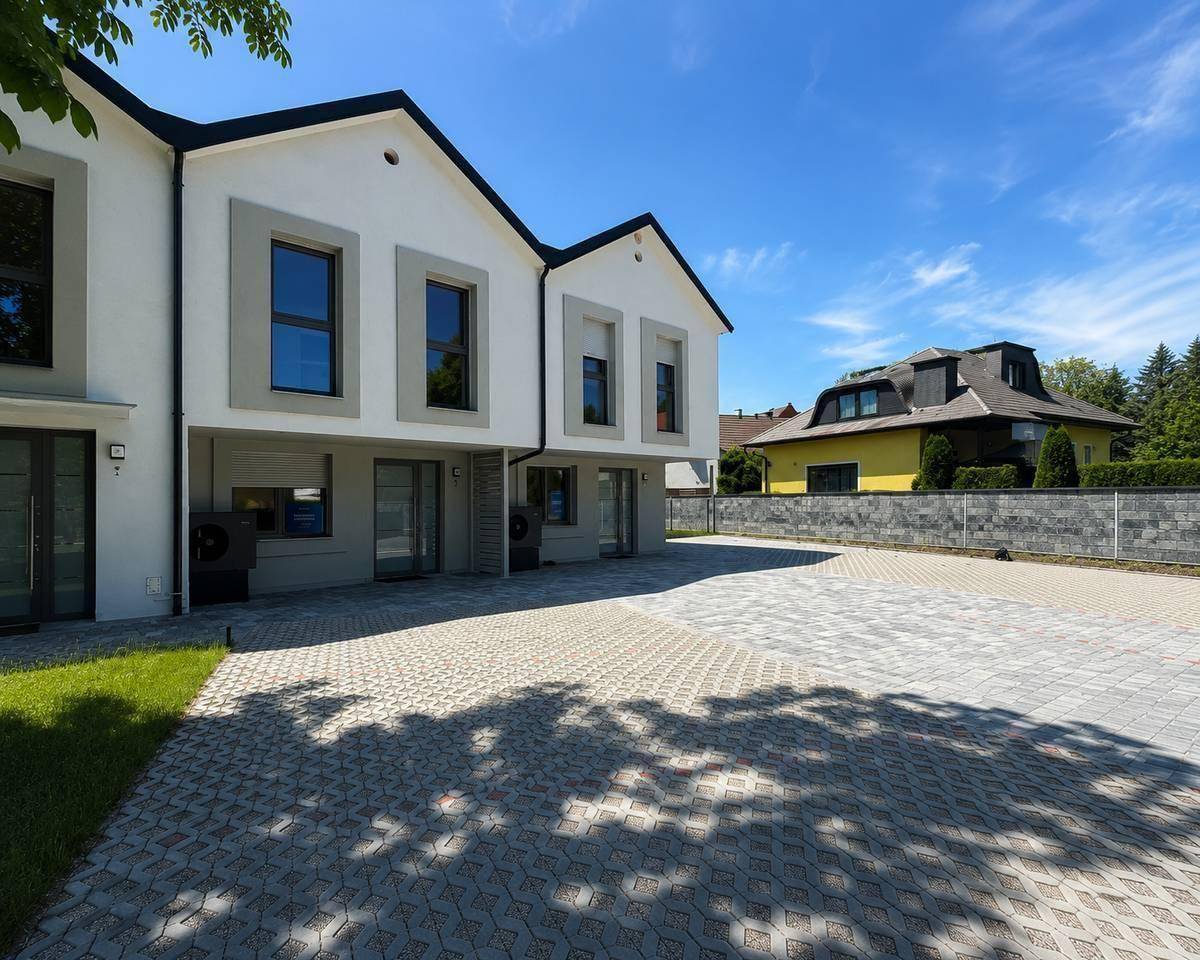 Moderne Reihenhäuser mit großzügigem gepflastertem Parkplatz unter blauem Himmel.