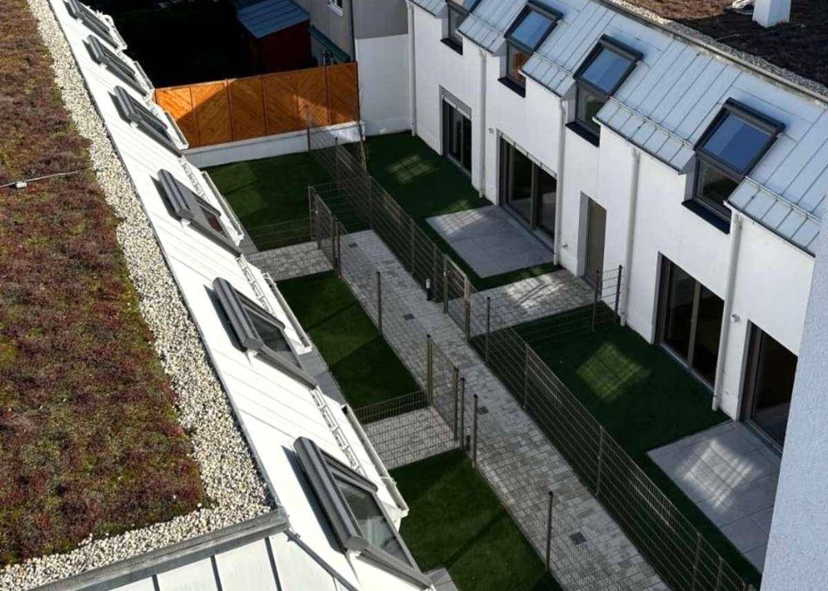 Blick von oben auf die privaten Gärten und gepflasterten Wege zwischen den modernen Wohngebäuden mit Gründach.