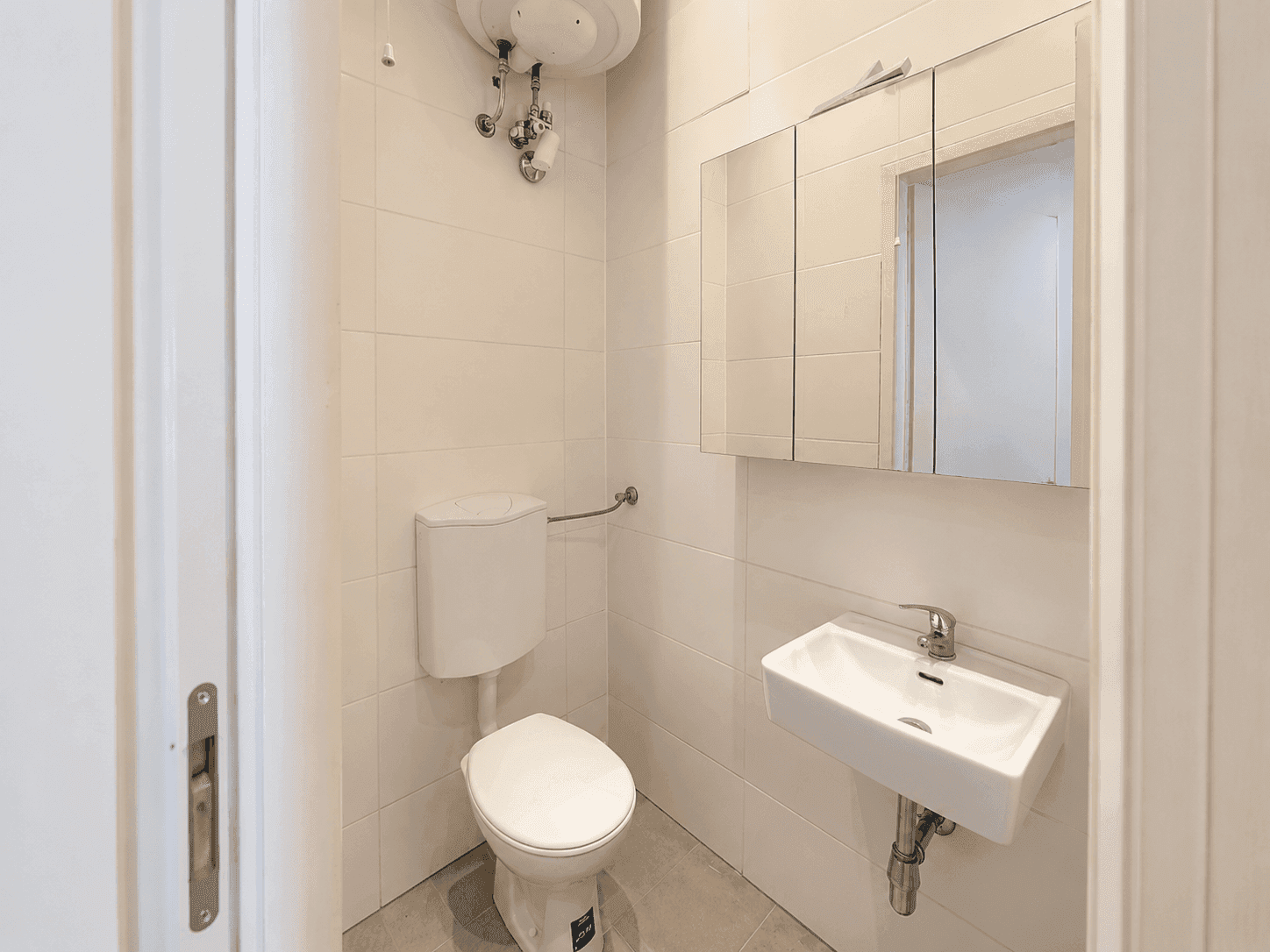 Modernes Gäste-WC mit weißen Fliesen, wandmontierter Toilette und einem kleinen Waschbecken mit Spiegelschrank.