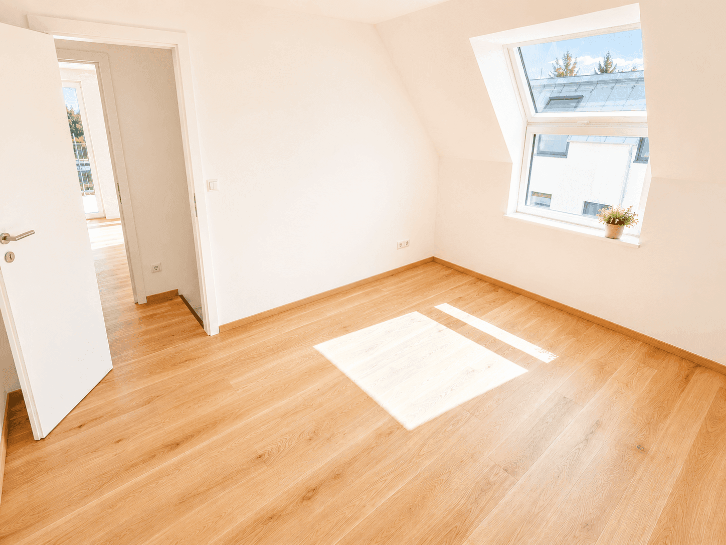 Helles Zimmer im Dachgeschoss mit Holzfußboden, weißen Wänden und großem Dachfenster für viel Tageslicht.