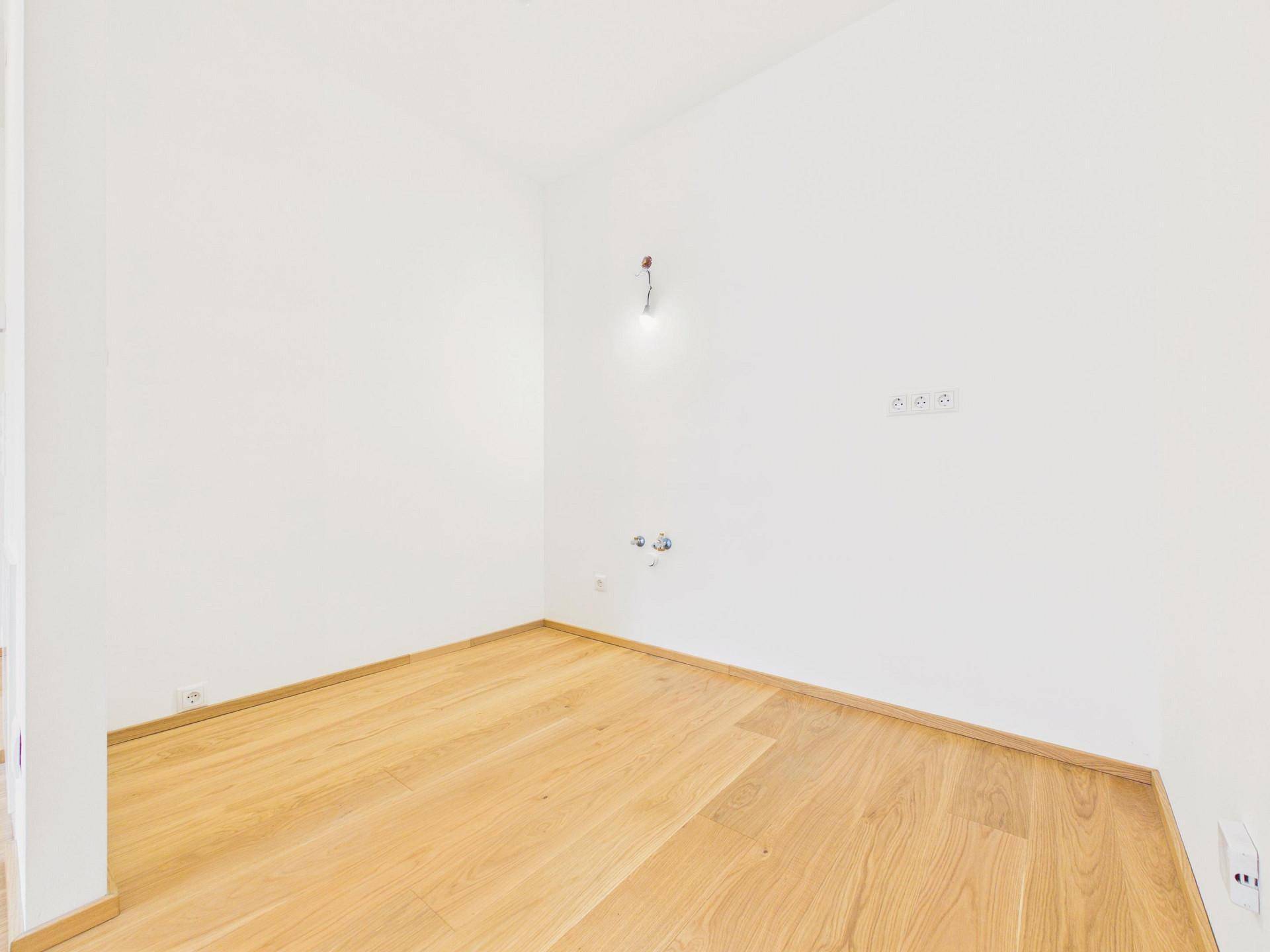 Eine Ecke des zukünftigen Küchenbereichs mit notwendigen Anschlüssen und hellem Holzboden.