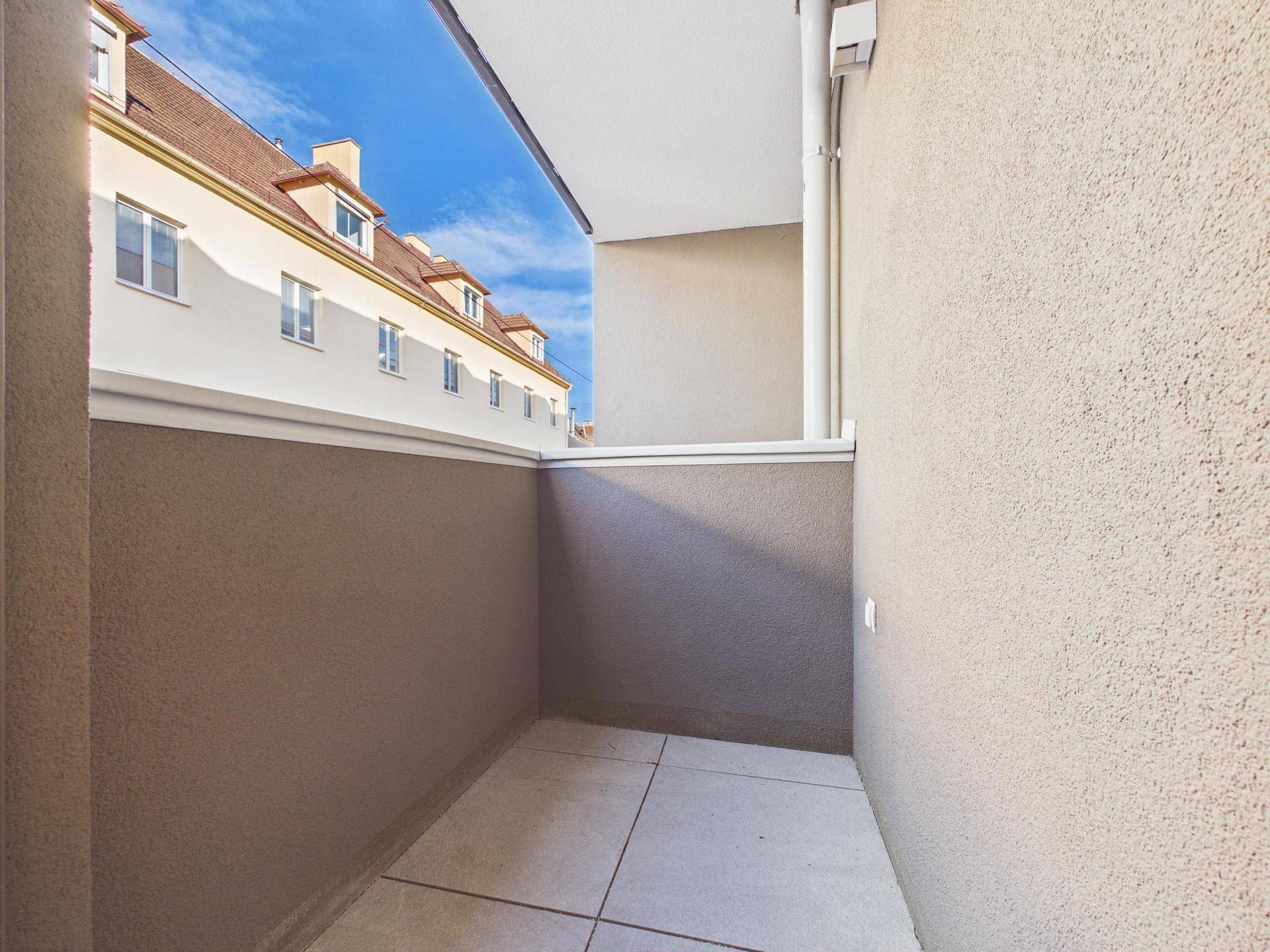 Kleiner, schmaler Balkon mit Fliesenboden und Blick auf die umliegenden Gebäude.