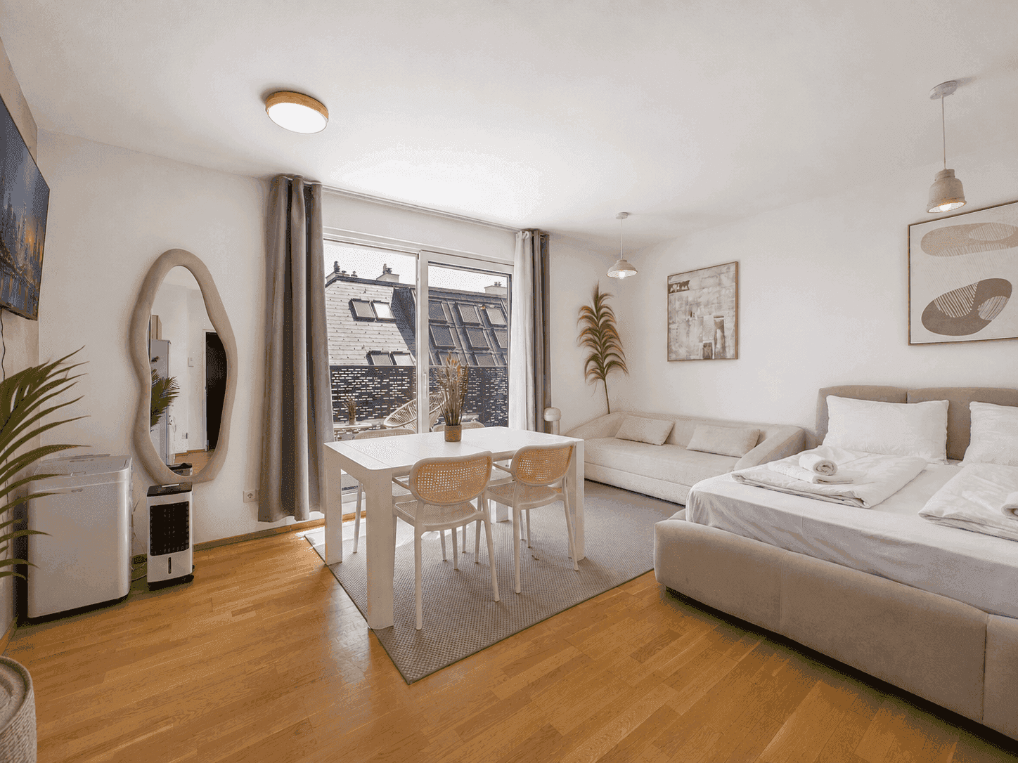 Geräumiger Wohnbereich mit Esstisch, Sofa und Bett, ausgestattet mit modernen Möbeln und Holzboden.