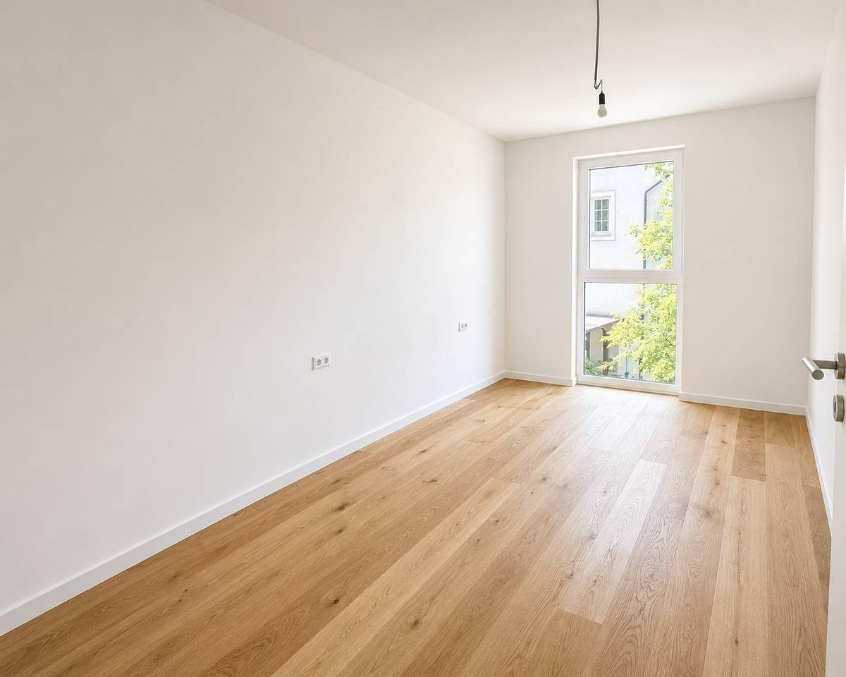 Helles Zimmer mit Holzboden und einem großen Fenster, das viel Tageslicht bietet.