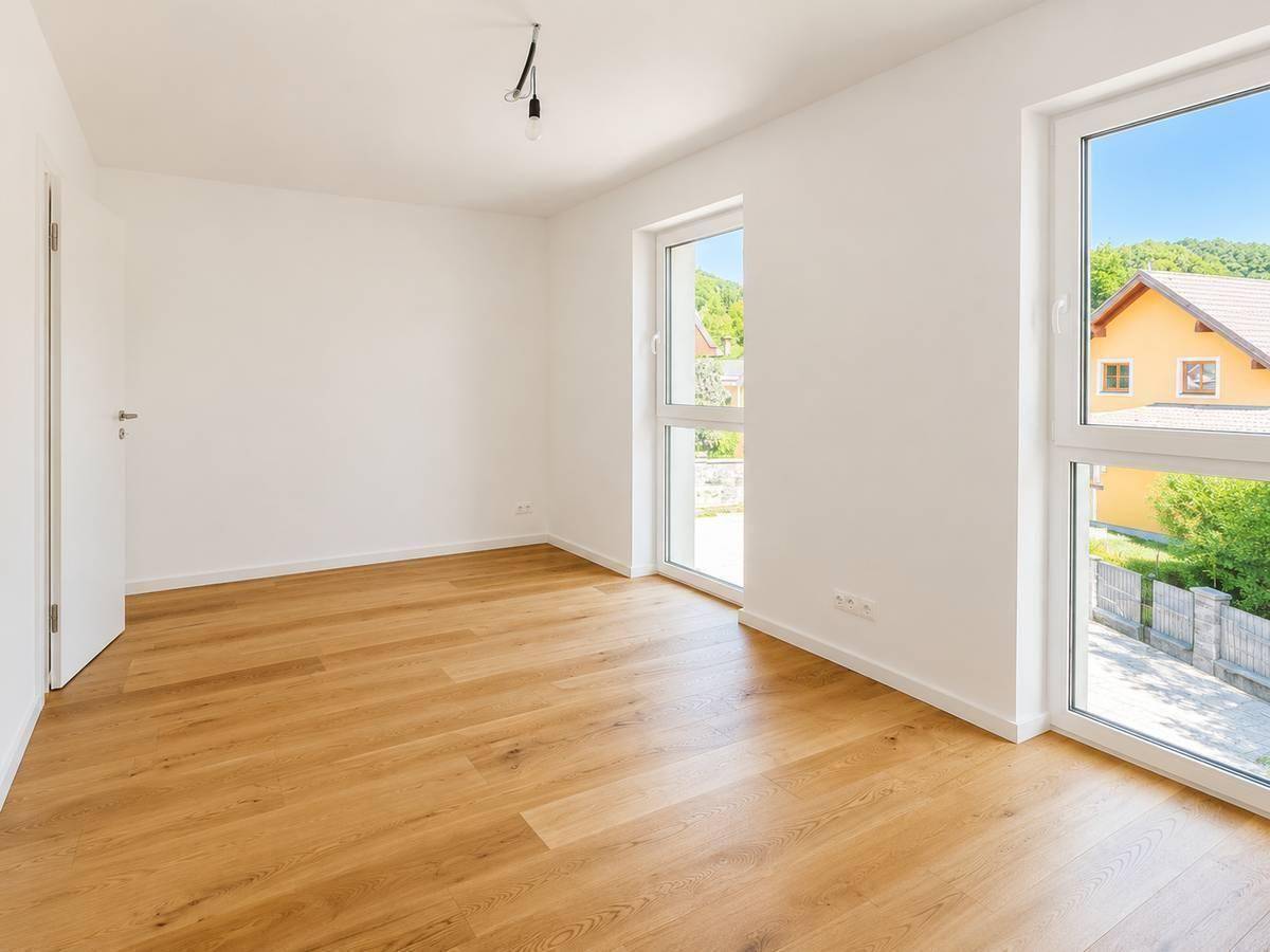 Geräumiges Schlafzimmer mit hellem Parkettboden und zwei großen Fenstern für viel Tageslicht.
