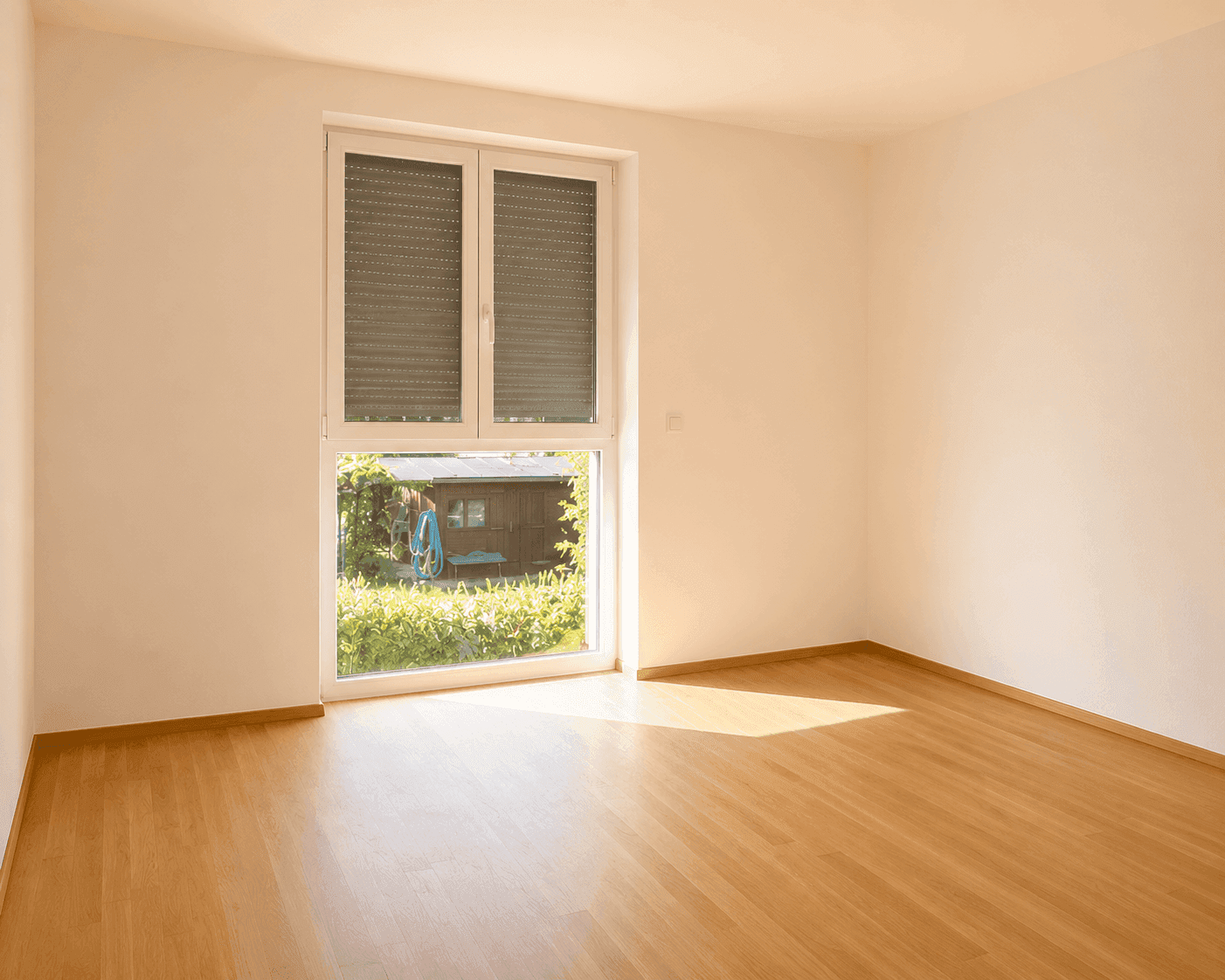 Helles Zimmer mit Holzboden und großem Fenster mit Blick auf einen Gartenschuppen.