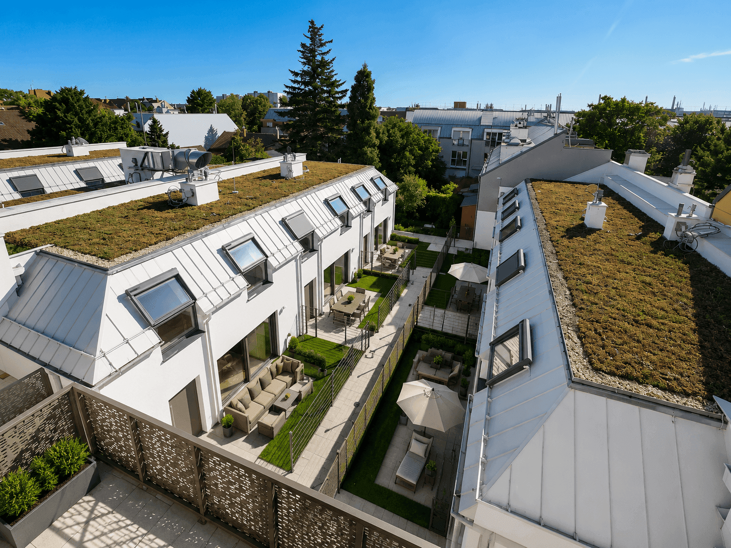 Begrünter Innenhof mit privaten Gärten, möblierten Terrassen und Sonnenschirmen zwischen den modernen Gebäuden.