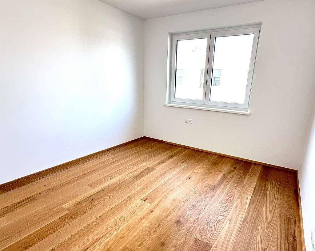 Helles, leeres Schlafzimmer mit Eichenparkett und großem Fenster, ideal für individuelle Einrichtung.