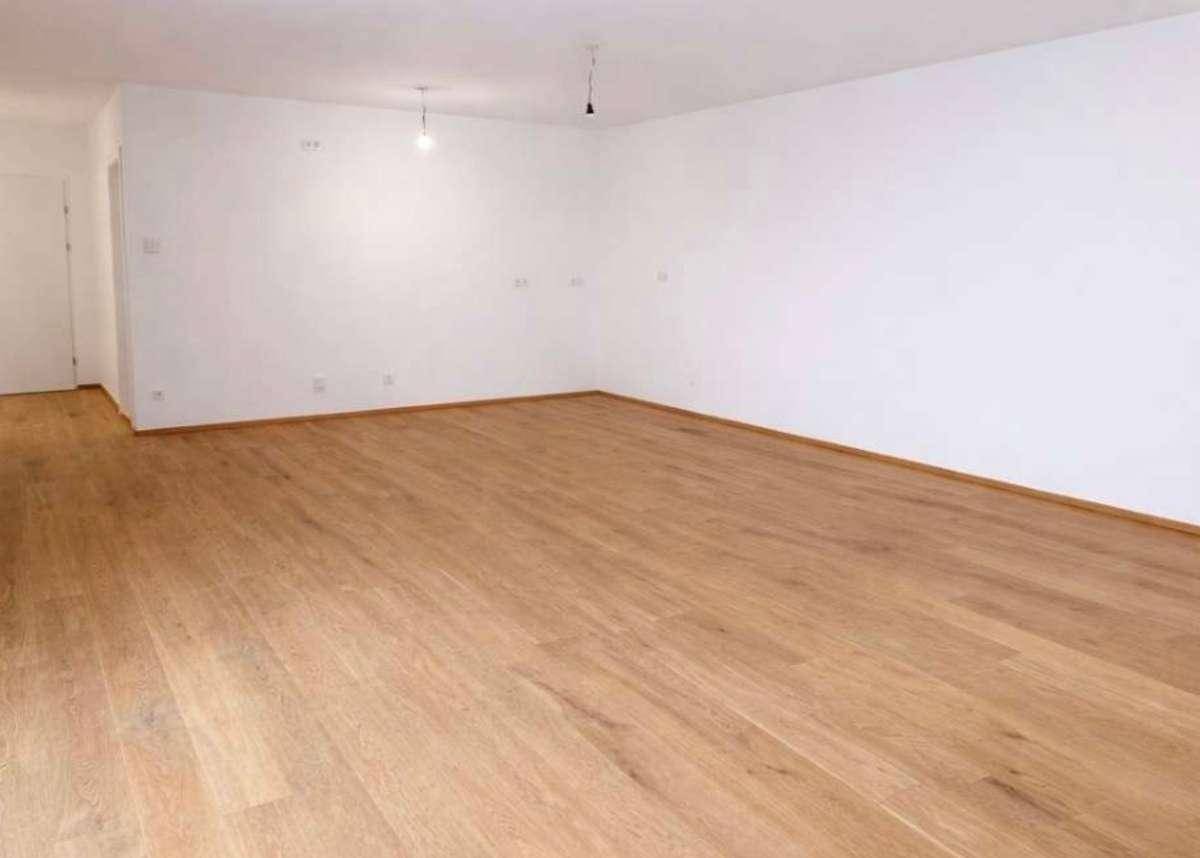 Geräumiges, leeres Wohnzimmer mit hellem Parkettboden und weißen Wänden.