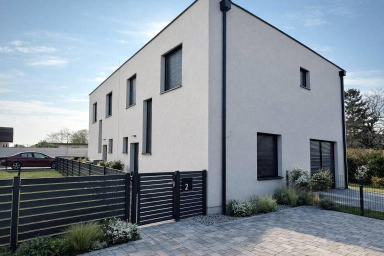 Modernes Einfamilienhaus mit weißer Fassade, dunklen Fenstern und gepflegtem Eingangsbereich.