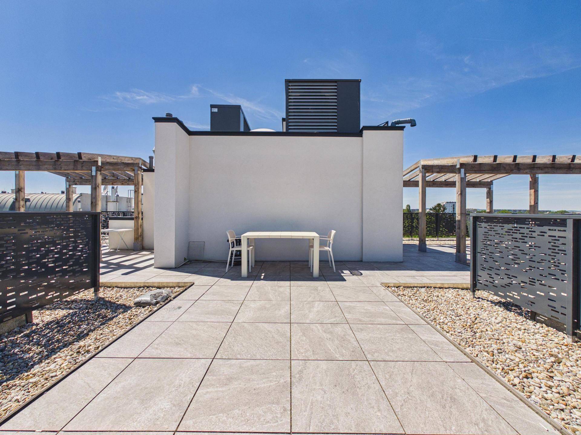 Geräumige Dachterrasse mit Fliesenboden und Sitzgelegenheit unter blauem Himmel.