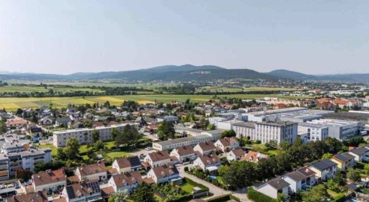 Weitläufige Landschaft mit Wohnsiedlungen und Bergen im Hintergrund unter blauem Himmel.