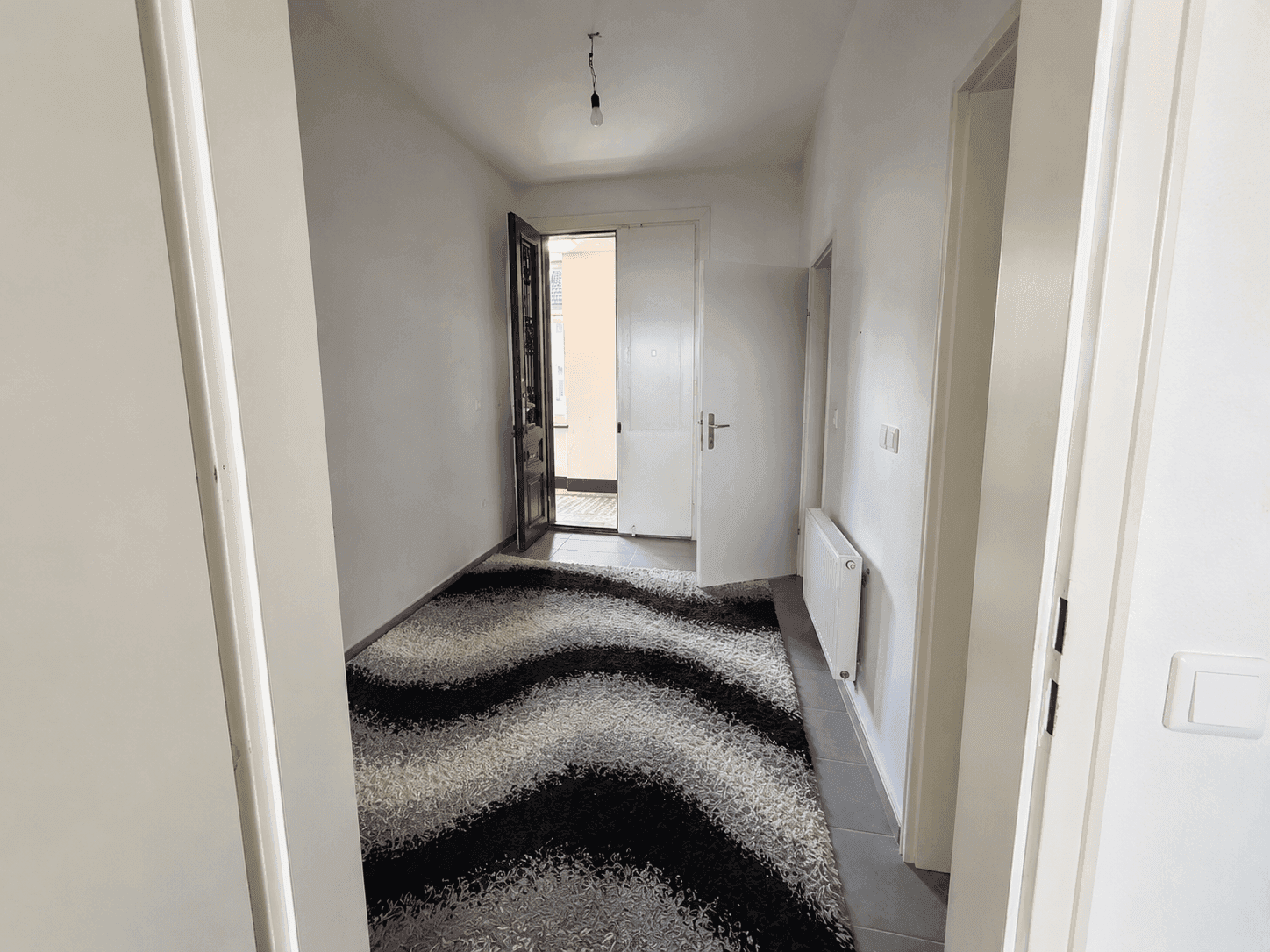 Heller Flur mit modernem Teppich und Zugang zu weiteren Zimmern der Wohnung.