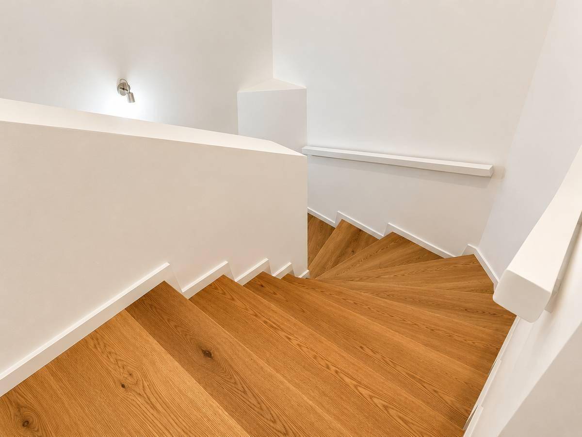 Moderne Holztreppe mit weißem Geländer, die die verschiedenen Etagen des Hauses verbindet.