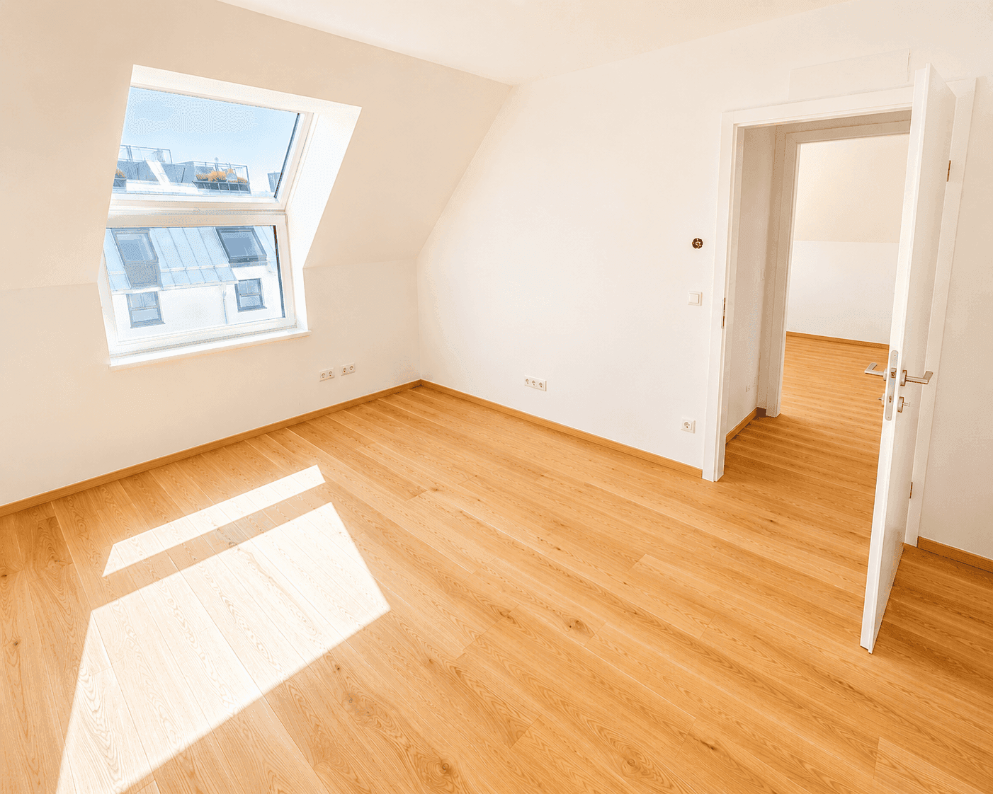 Helles Zimmer im Dachgeschoss mit Holzfußboden, weißen Wänden und großem Dachfenster, ideal als Schlafzimmer.